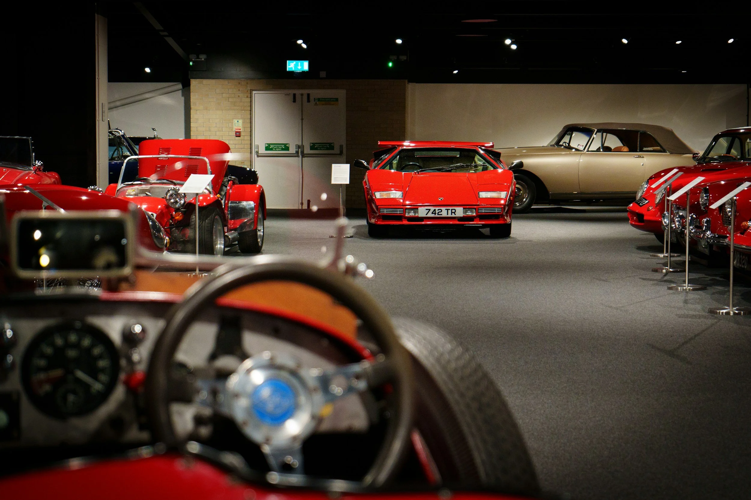 A collection of vintage and classic cars displayed in a museum, with a red Lamborghini in the center and other old vehicles surrounding it.