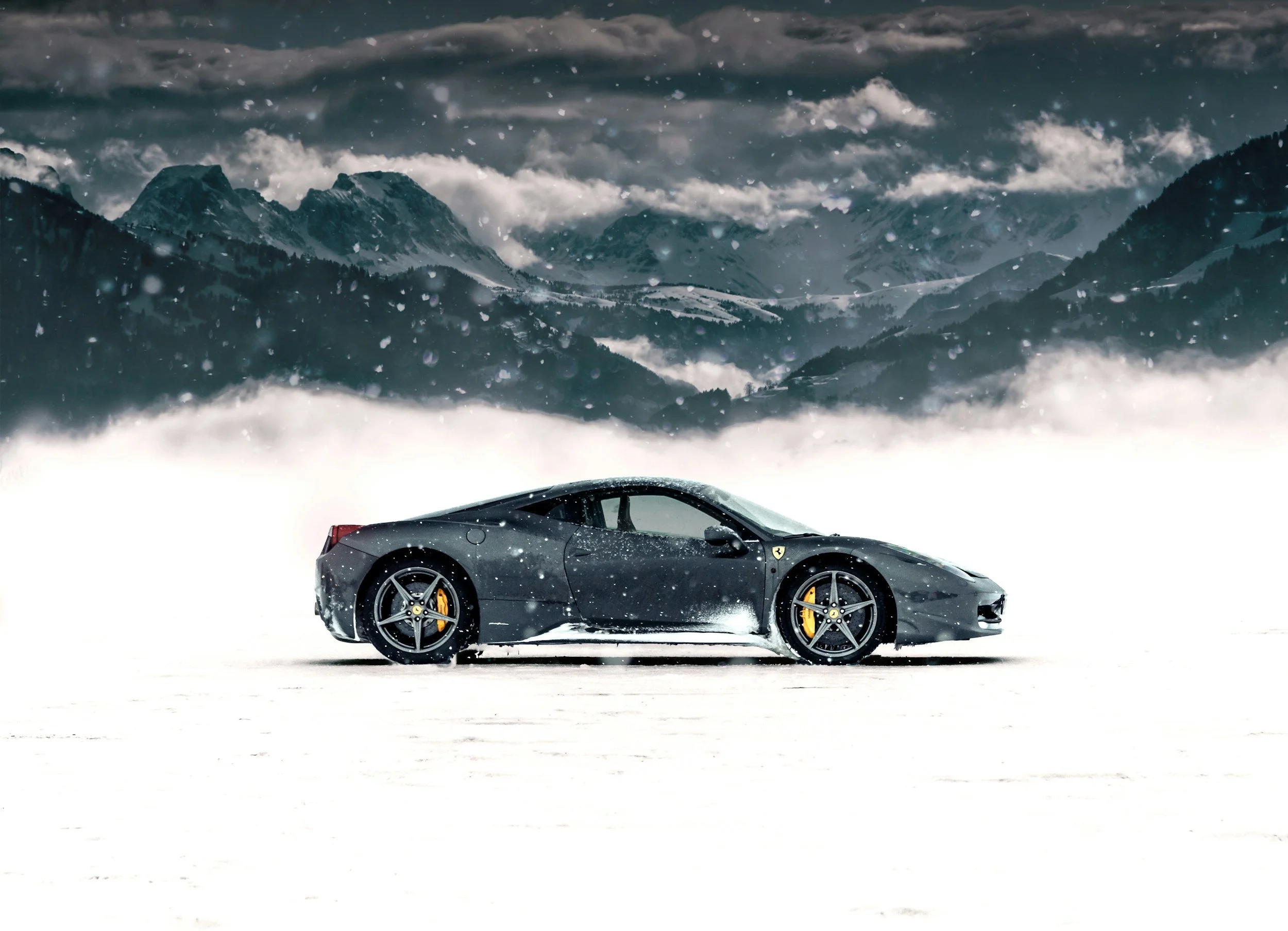 car driving in snow yellow brakes mountains in background clouds and snow