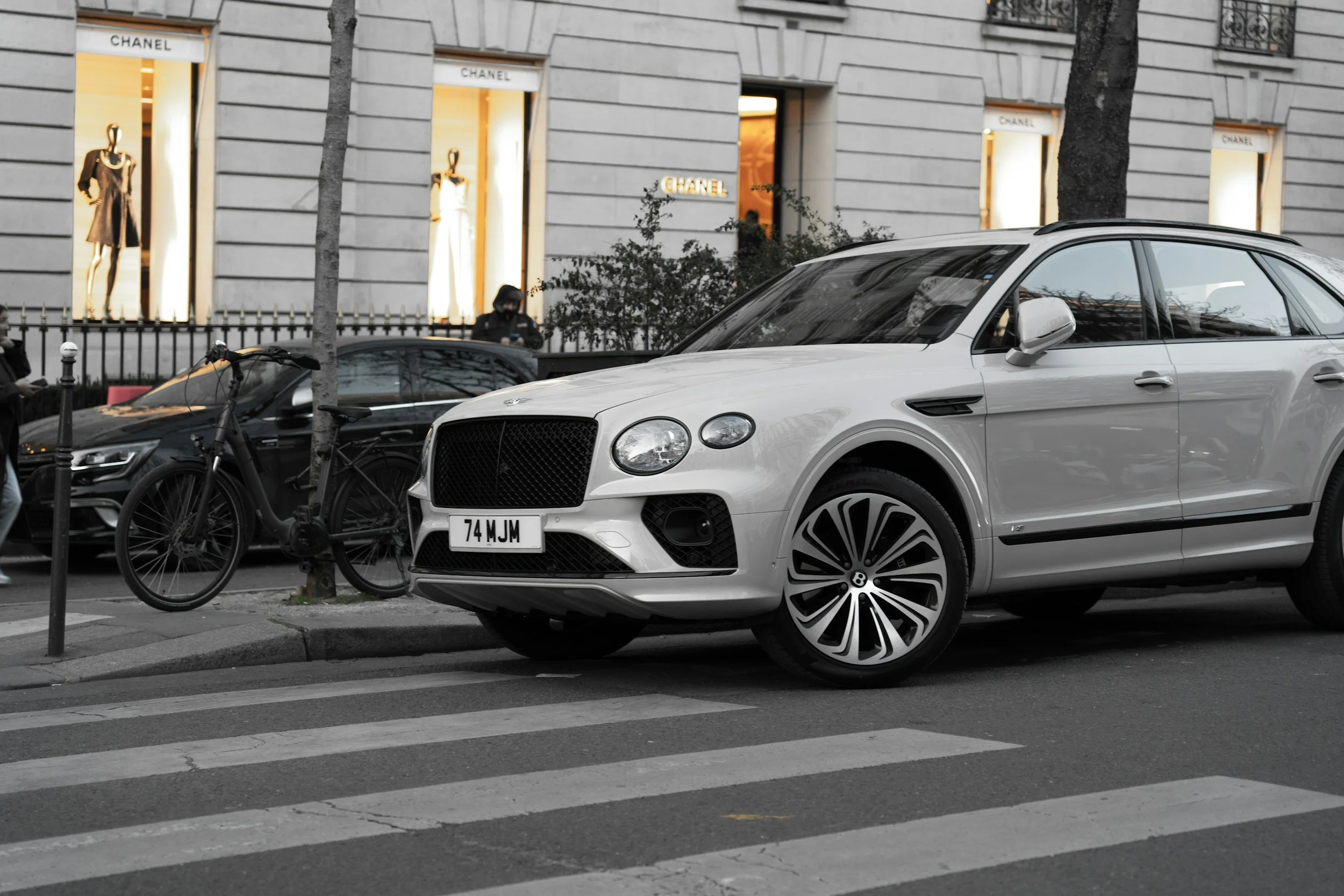 white suv bentley car parked in city along the sidewalk