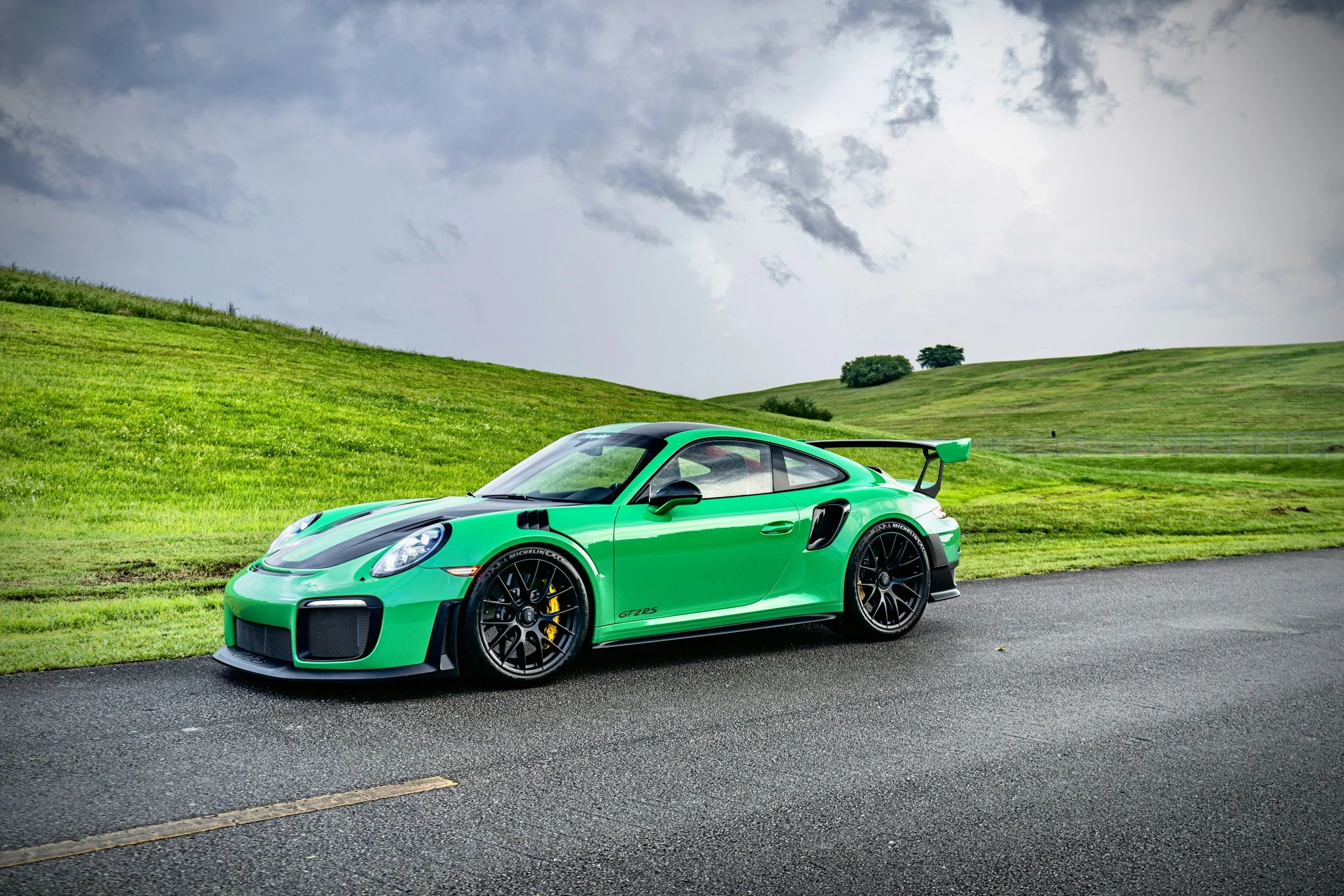 2 door car bright neon green parked along road with really green grass and yellow brakes
