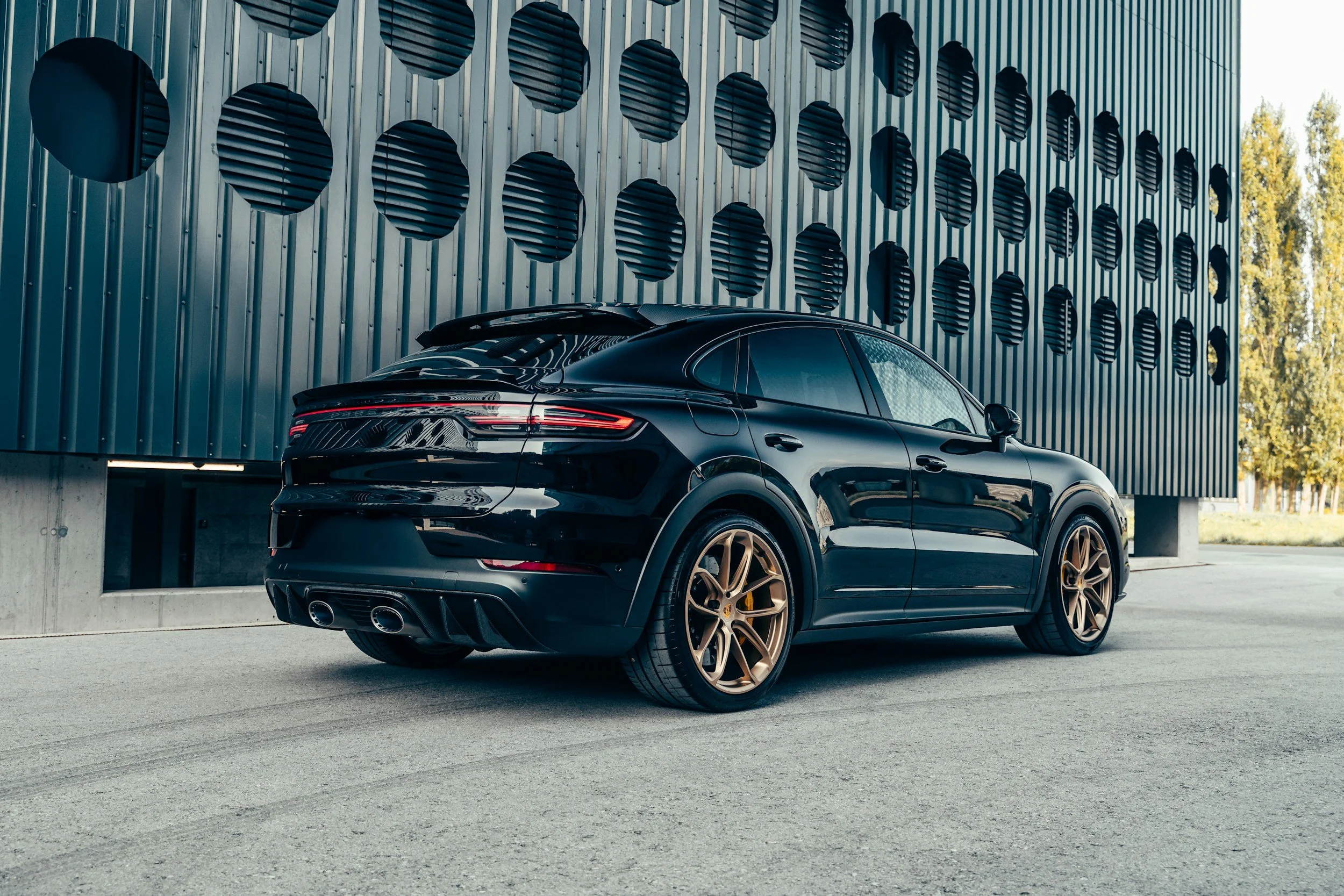 black or dark blue suv 4 door vehicle gold wheels parked against wall with a bunch of large artsy holes