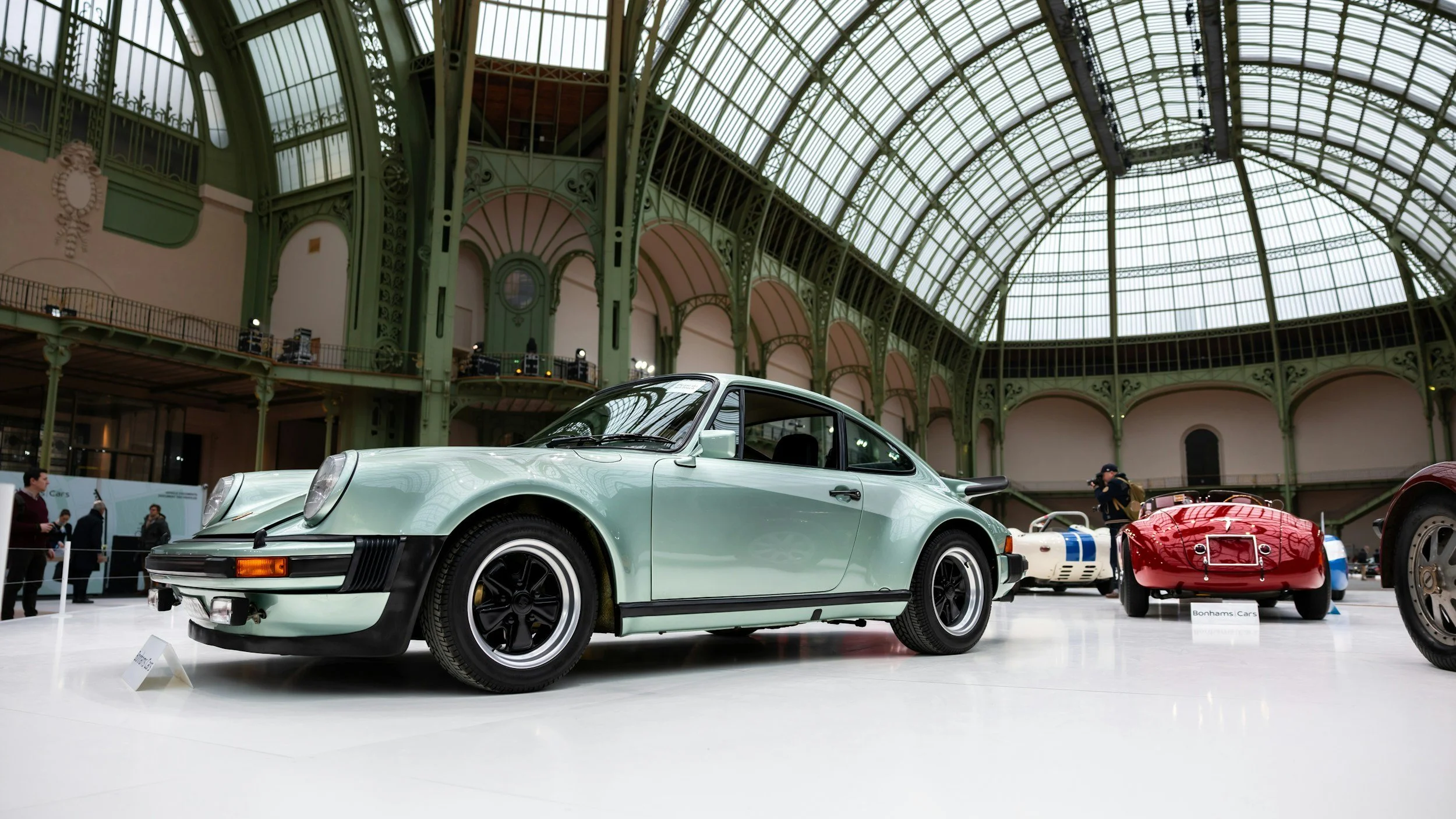 LIGHT GREEN CAR RED CAR WHITE CAR WITH BLUE STRIPS IN LARGE BUILDING WITH GLASS ROOF