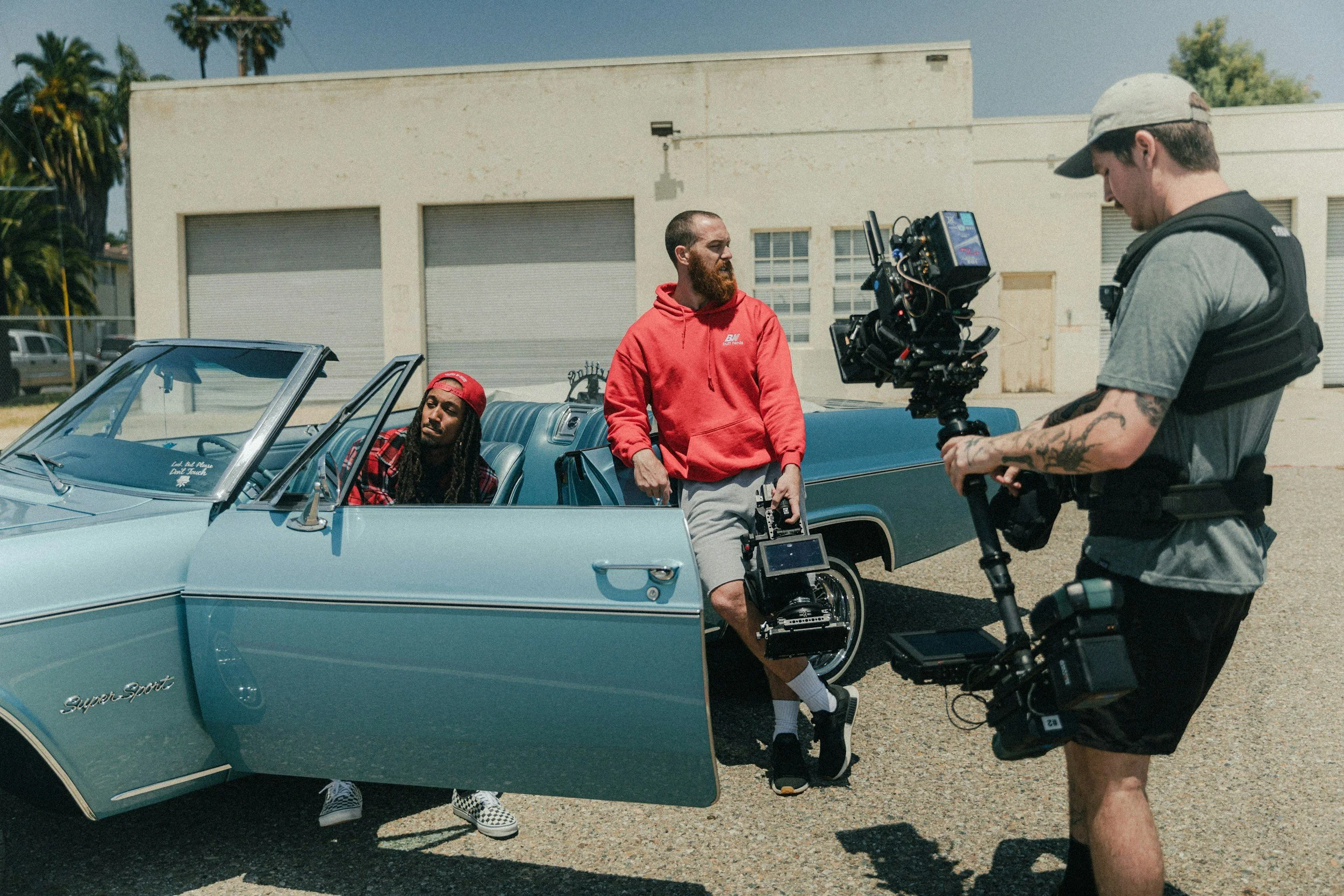 3 people one holding camera the other filming while the other is sitting in car getting ready for filming