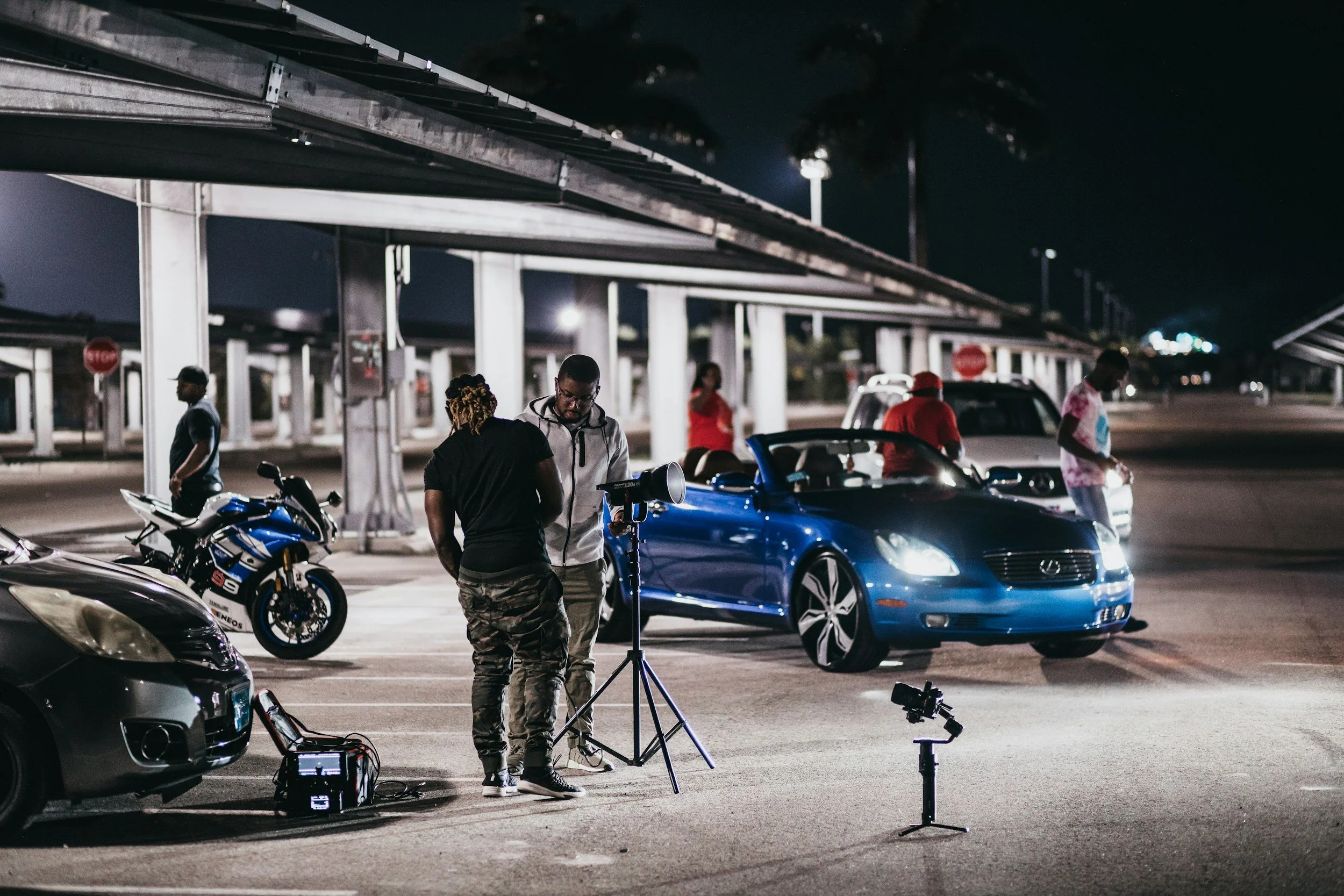 6 peoplle shooting a car scene interview blue car 6 spoke wheels motorcycle and 2 other cars
