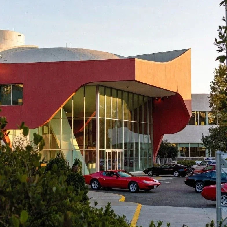 large art deco art buidling with red blue green white Ferrari outside in front of car museum with pnw car smart