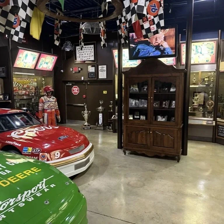 green and red race car with trophies shelves car parts flgas hanging from the ceiling car racing display at car museum with pnw car smart