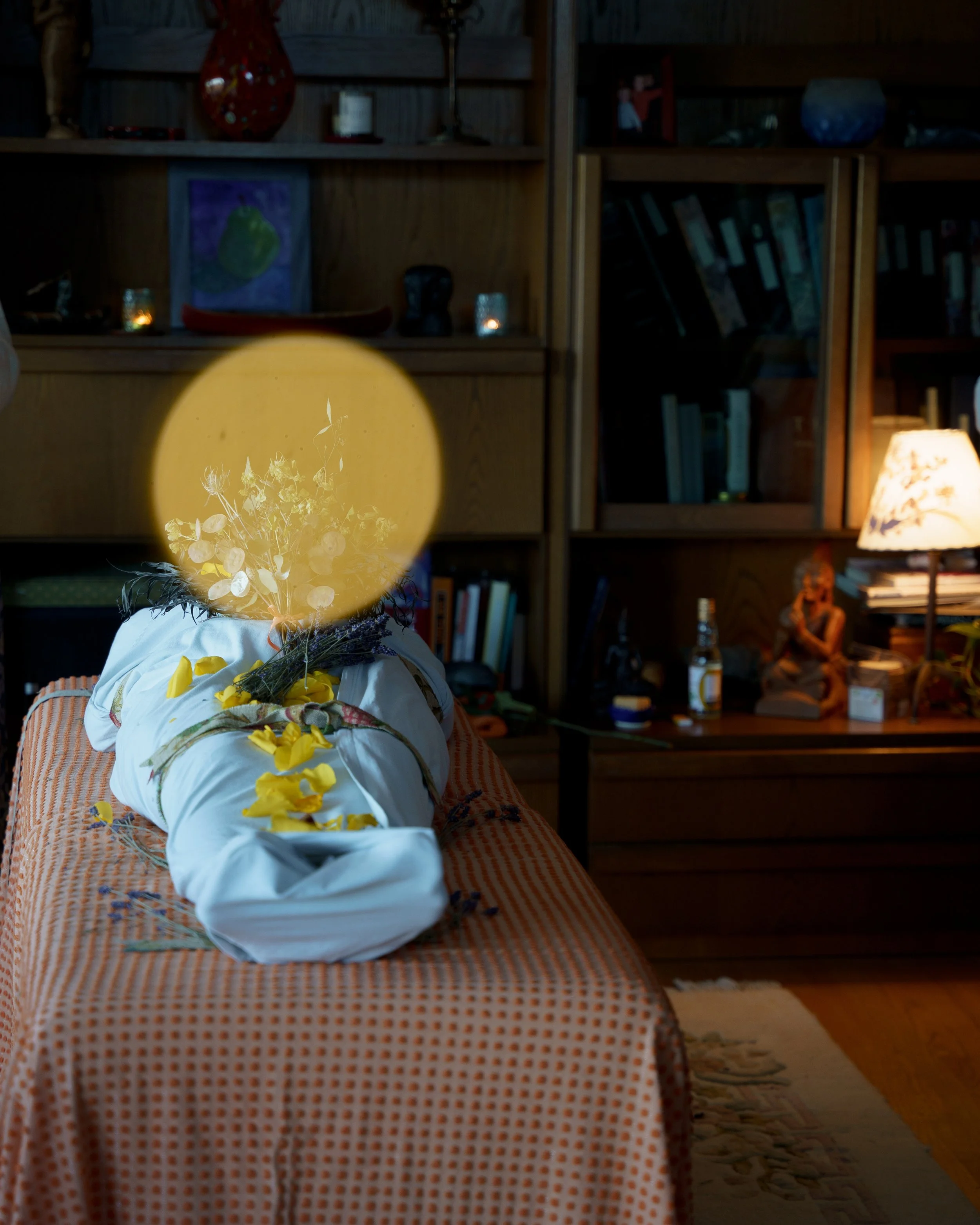 A shrouded body lying in honour on a table, decorated with flowers.