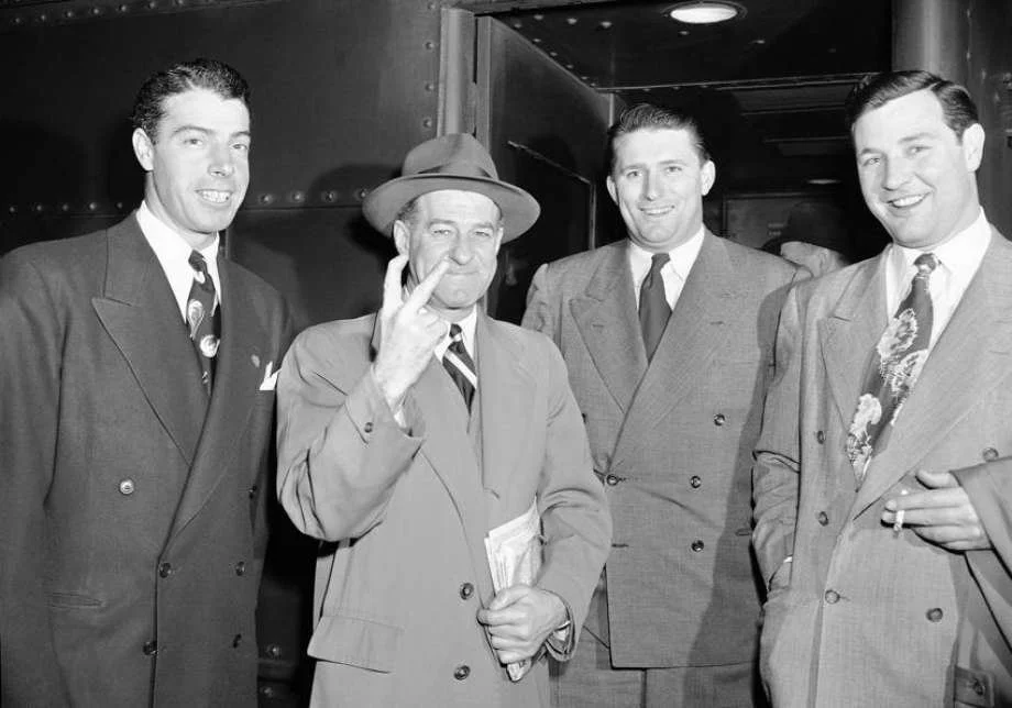New York Yankee manager Stanley "Bucky" Harris, second from left, holds up two fingers, signifying his intention of bringing his team home in front for the second consecutive season, as Harris, Joe DiMaggio, left, Frank "Spec" Shea, second from right