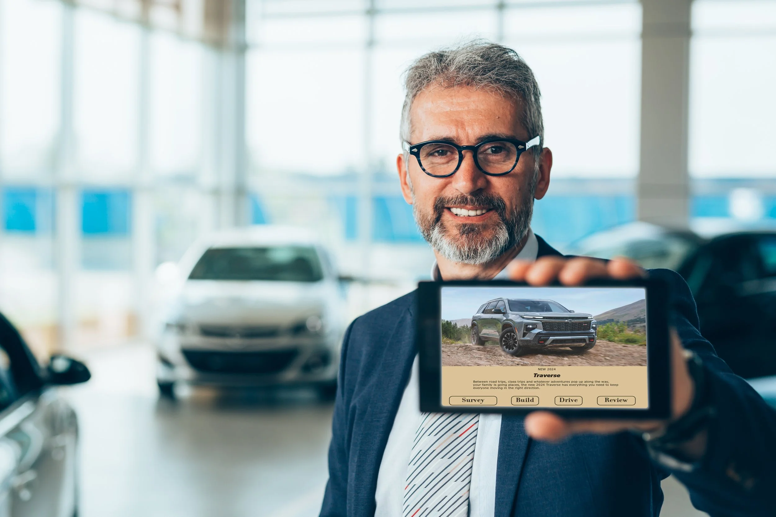 A man with glasses and gray hair smiling and taking a photo of a car with his smartphone inside a car dealership.