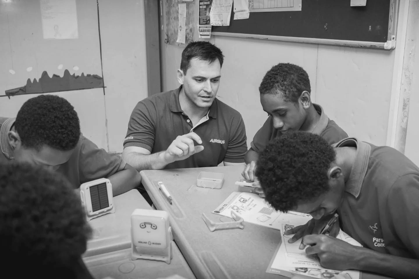 An Airbus engineer mentoring students through hands-on electronics assembly as part of a corporate volunteering program, demonstrating skills-based volunteering and cross-sector collaboration in STEM education.