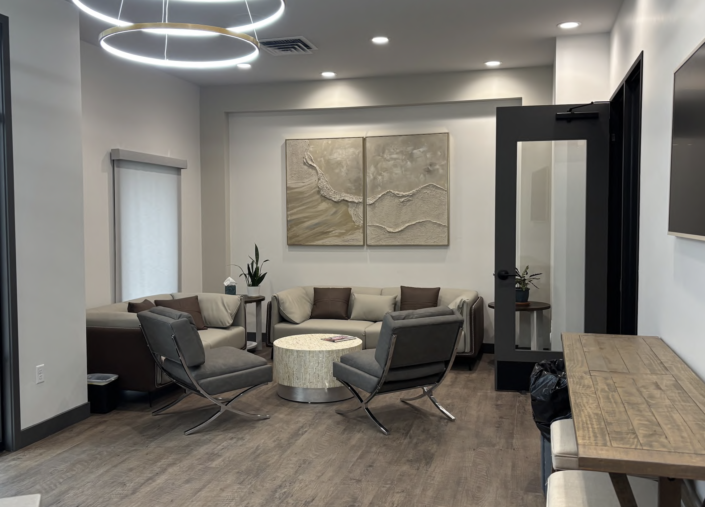 Whitehaven Dental modern waiting room with gray seating, a round coffee table, abstract wall art, and overhead circular lights.
