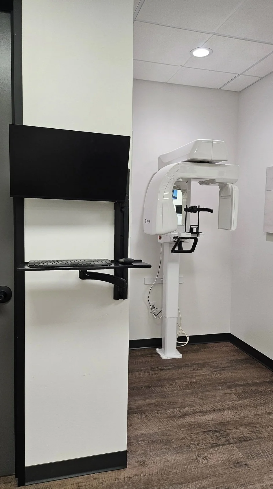 Medical imaging room with a large CT scanner and a computer station with a monitor and keyboard.