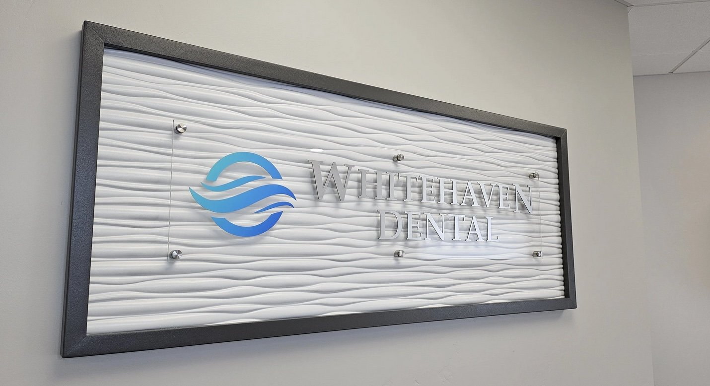 Wall sign for Whitehaven Dental with blue logo of waves and a circle.