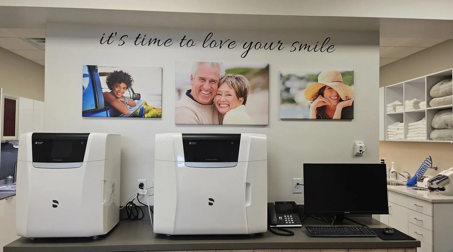 A wall with three framed photos of smiling people above two white medical devices on a counter. The wall has a quote: 'it's time to love your smile'.
