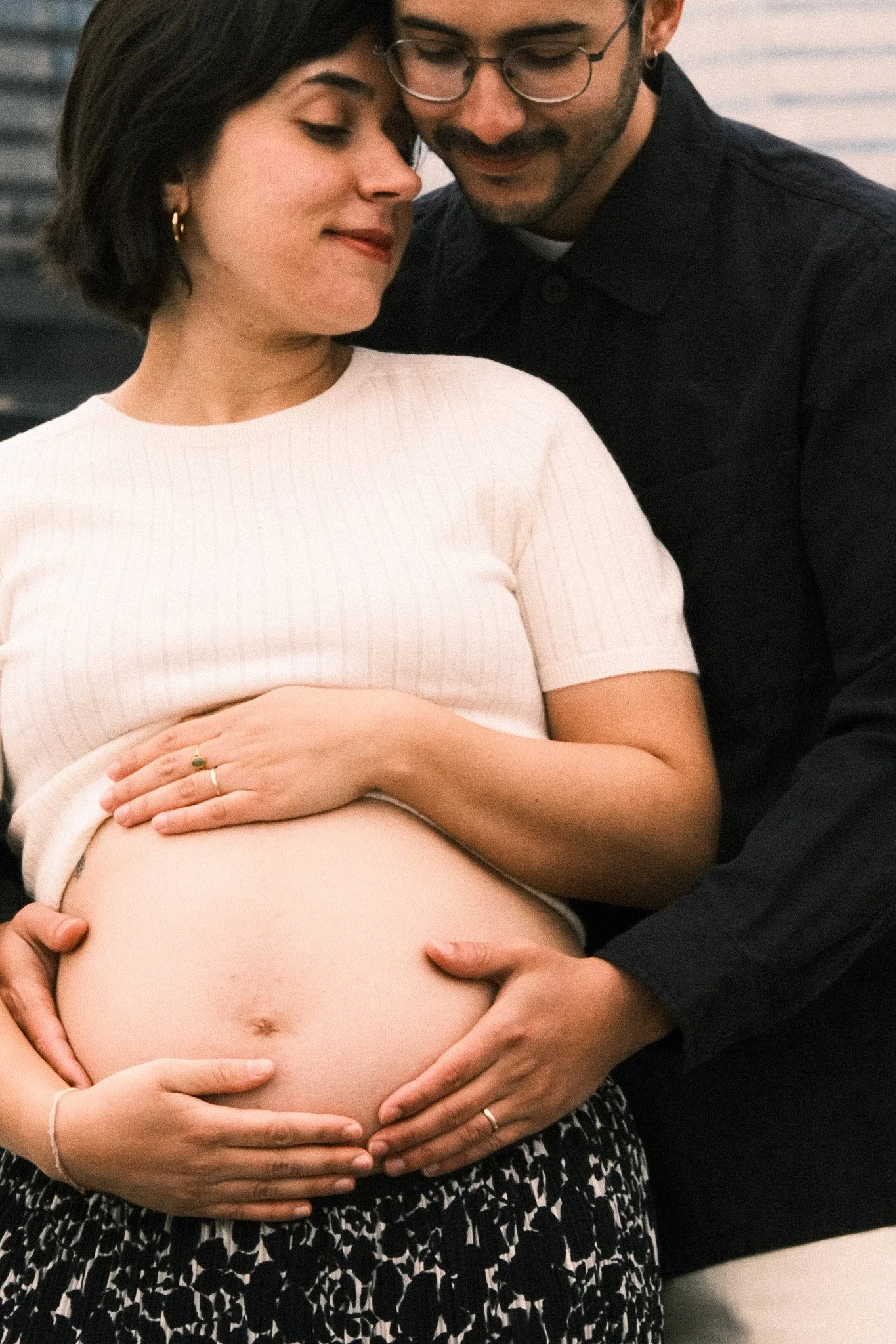 Une femme enceinte, soutenue par deux mains, et un homme qui la regarde avec tendresse, lors d'une séance de grossesse