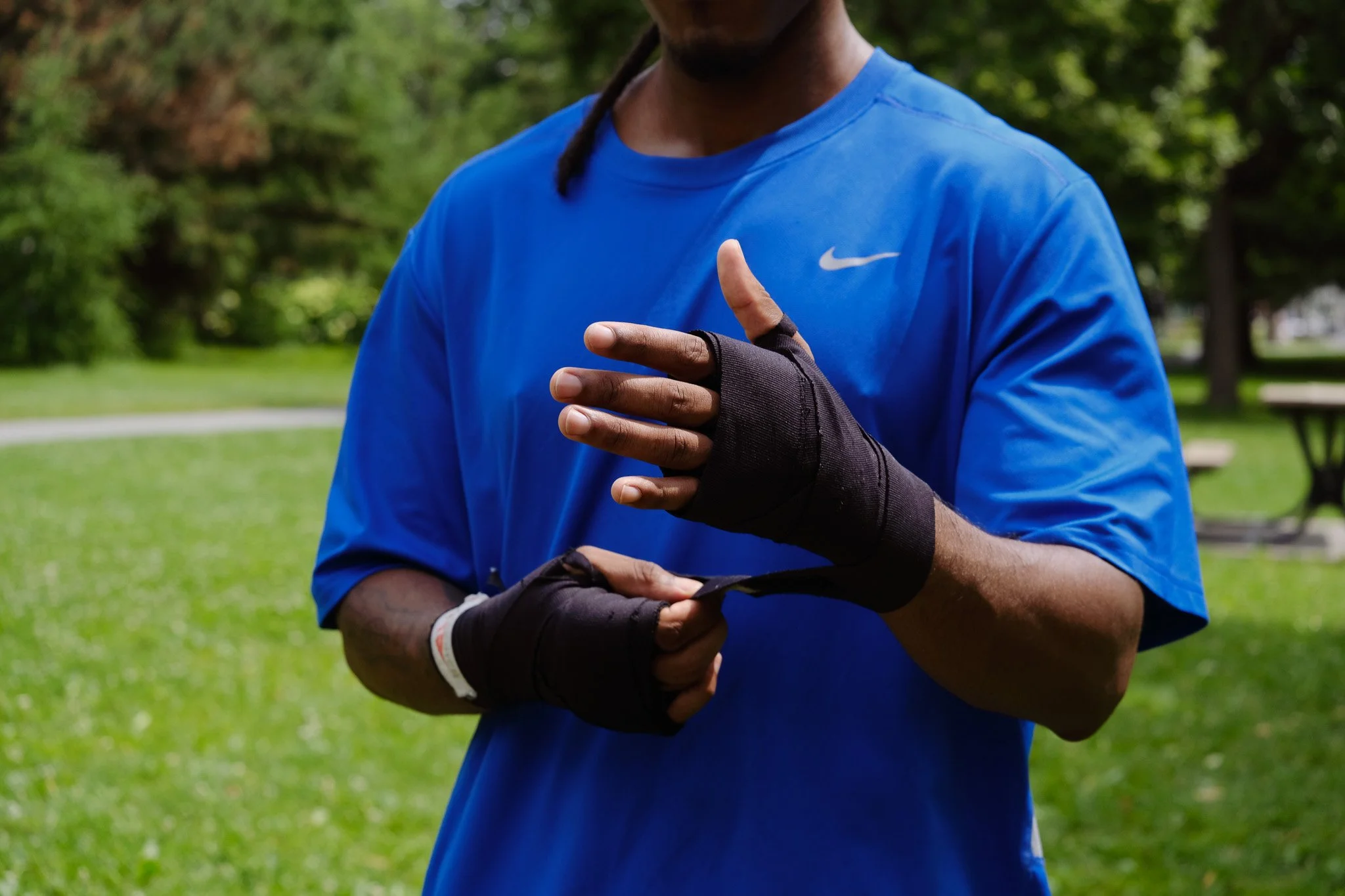 Homme vêtu d'un t-shirt bleu avec des gants de sport noirs, ajustant ses gants dans un parc vert.