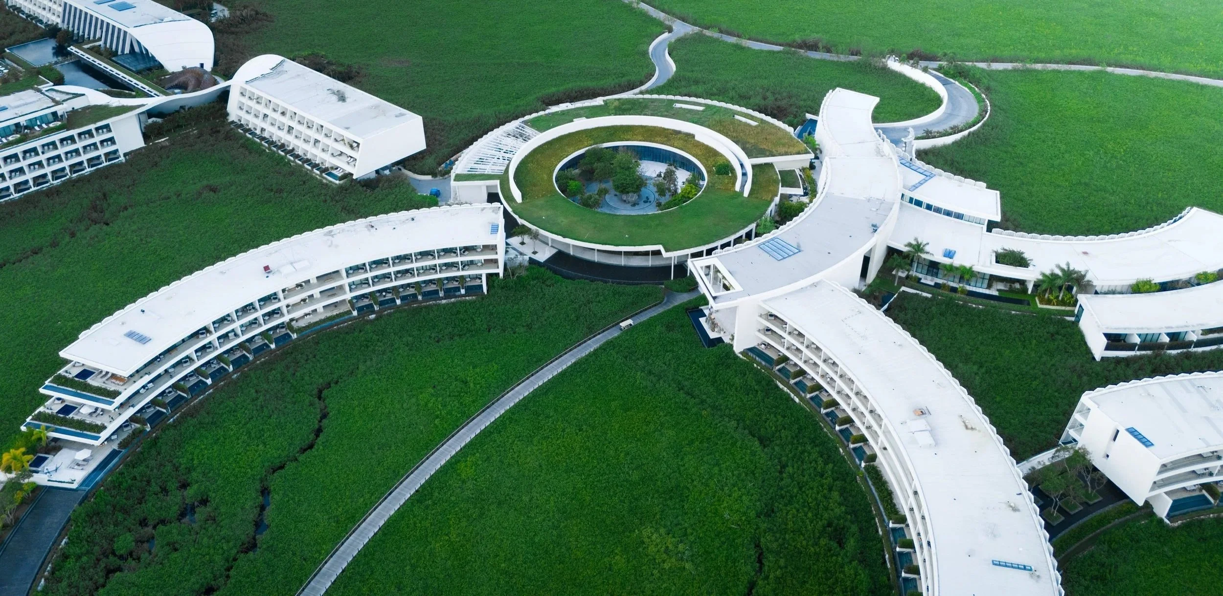 Aerial view of a modern, white building complex with curved structures and surrounding green lawns.