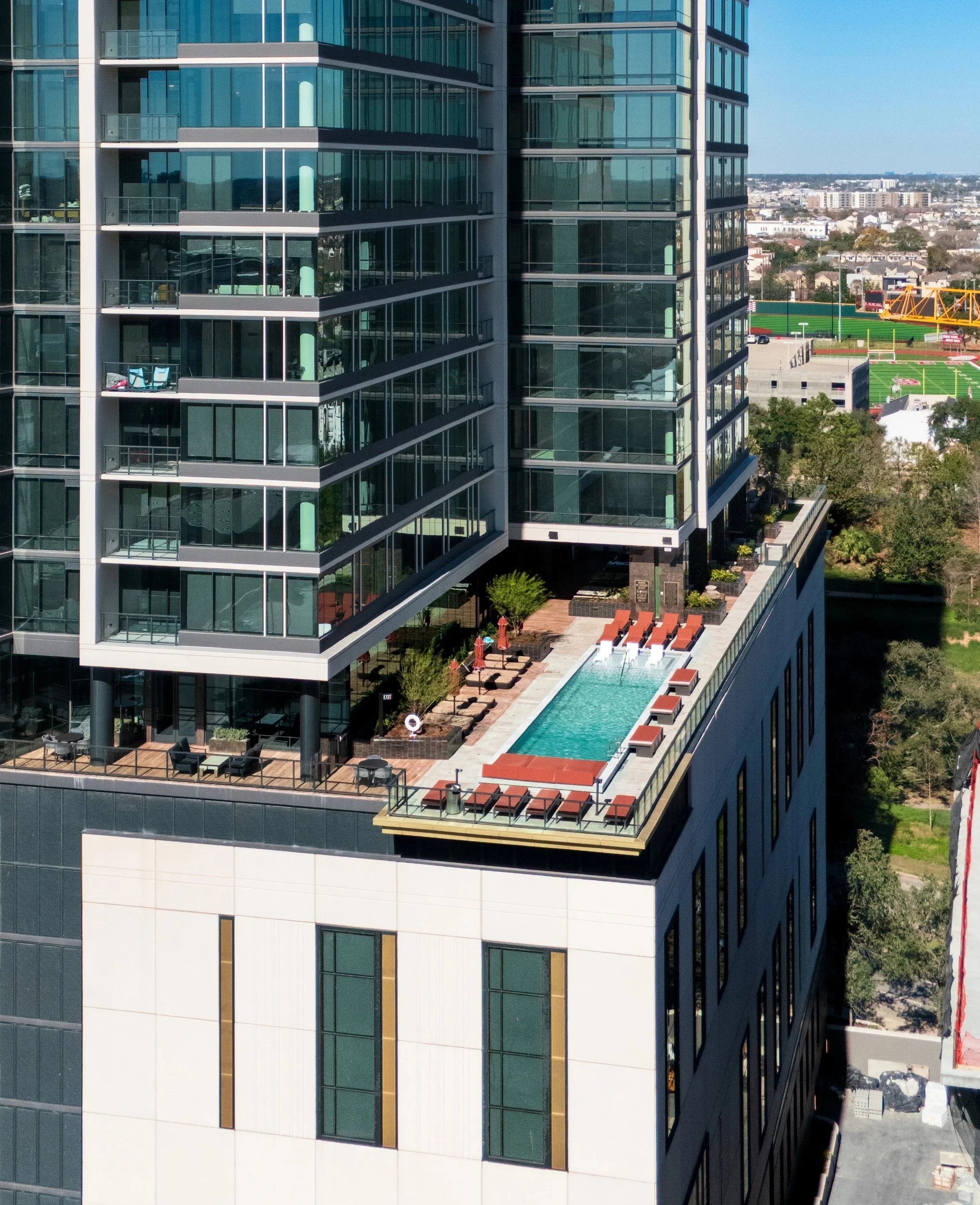High-rise building with cityscape in the background, featuring a rooftop swimming pool with lounge chairs and outdoor seating area.