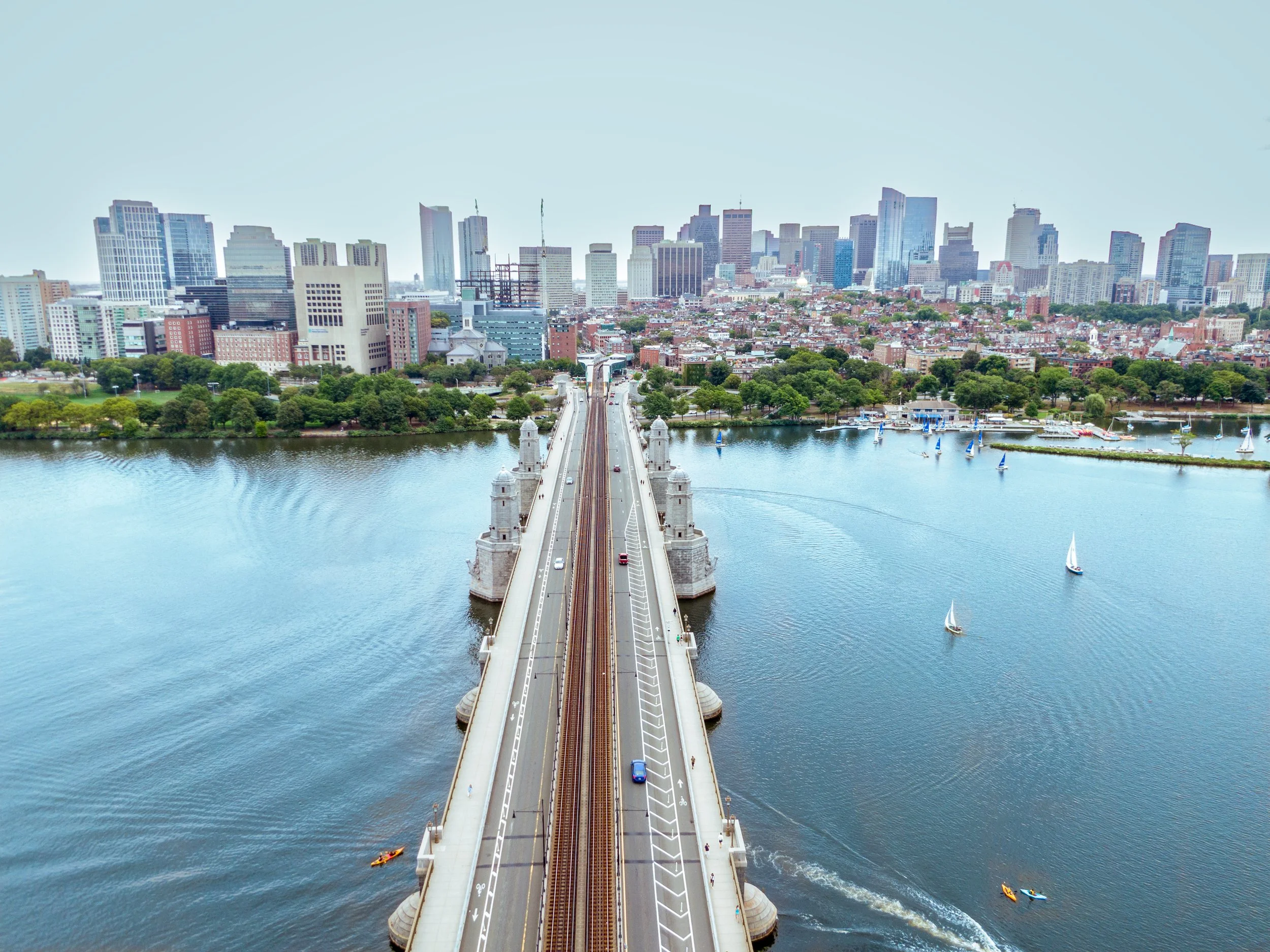 Aerial view of a city skyline with a river and a bridge crossing over it, sailboats on the river.