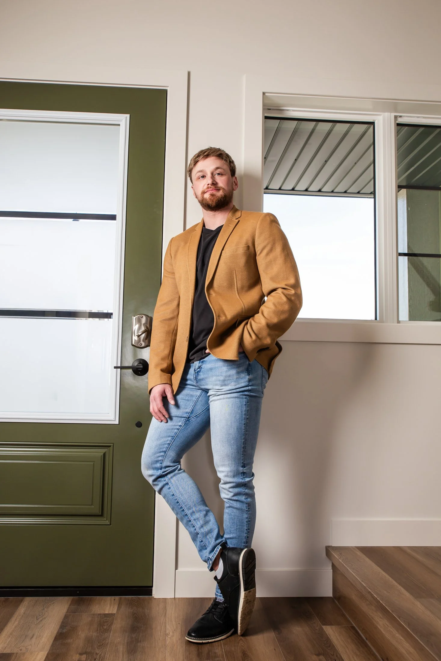 A man wearing a navy blue suit and white shirt standing in a modern house with large windows, greenery outside, and contemporary furniture inside.