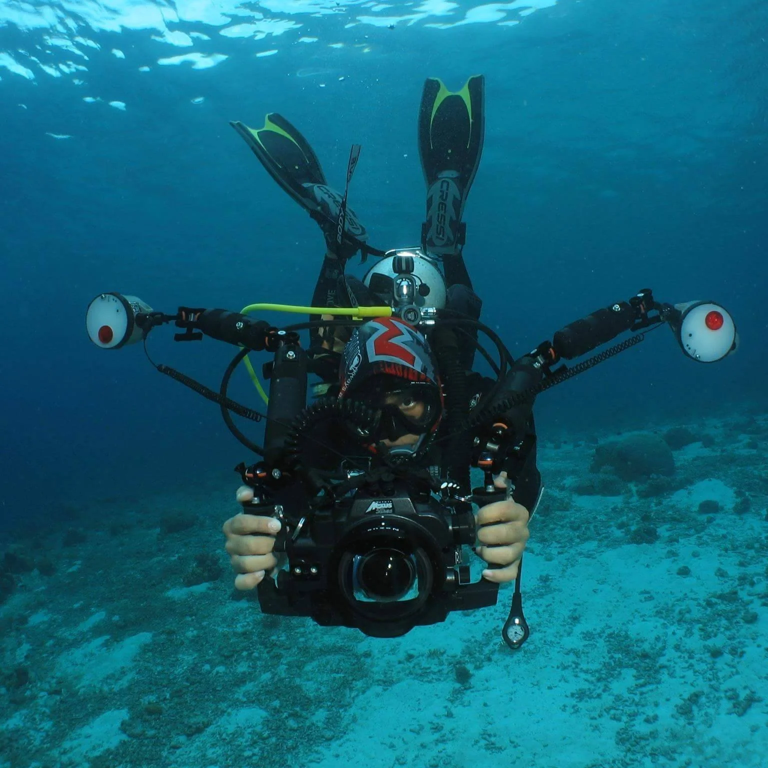 Underwater photographer with scuba gear and large camera housing, swimming in ocean.