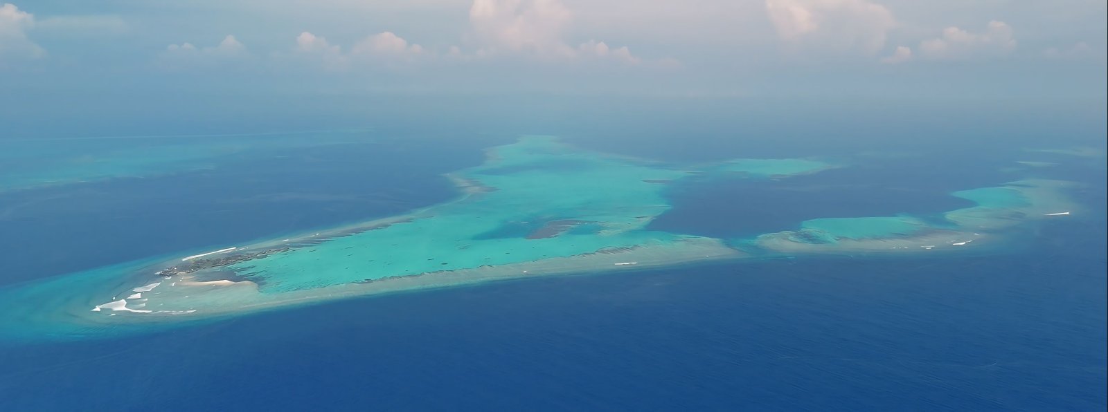Aerial view of a tropical island surrounded by turquoise and deep blue ocean waters.