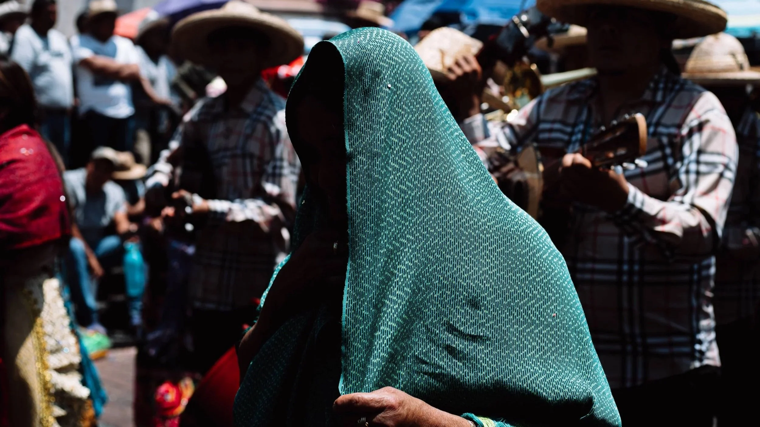 Mujer mexicana con rebozo color verde en la cabeza cubriéndose del sol en un día caluroso de verano durante fiestas patronales en Uruapan, Michoacán