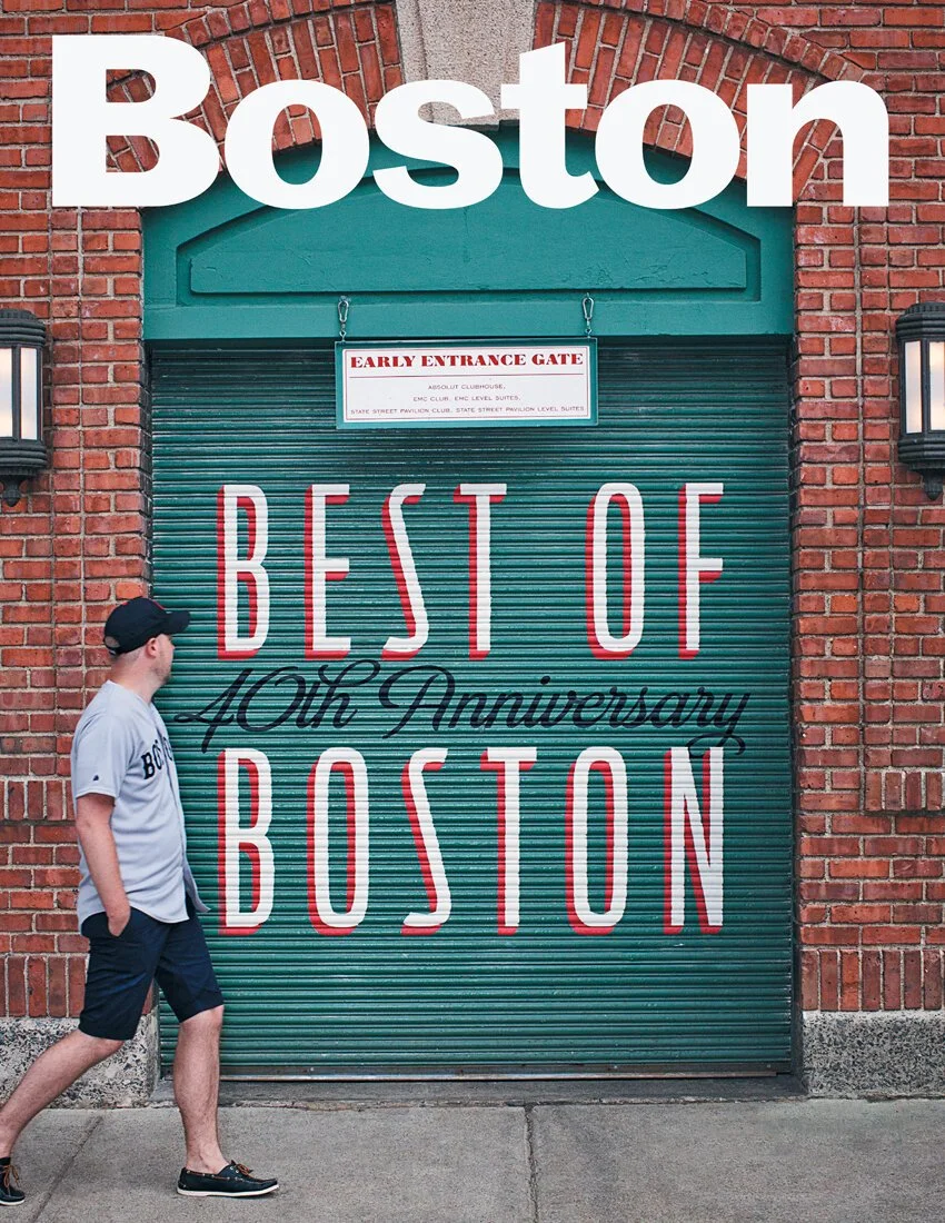 A person walking past a green garage door with text celebrating the 40th anniversary of Boston, with red brick walls on either side and two wall lamps.