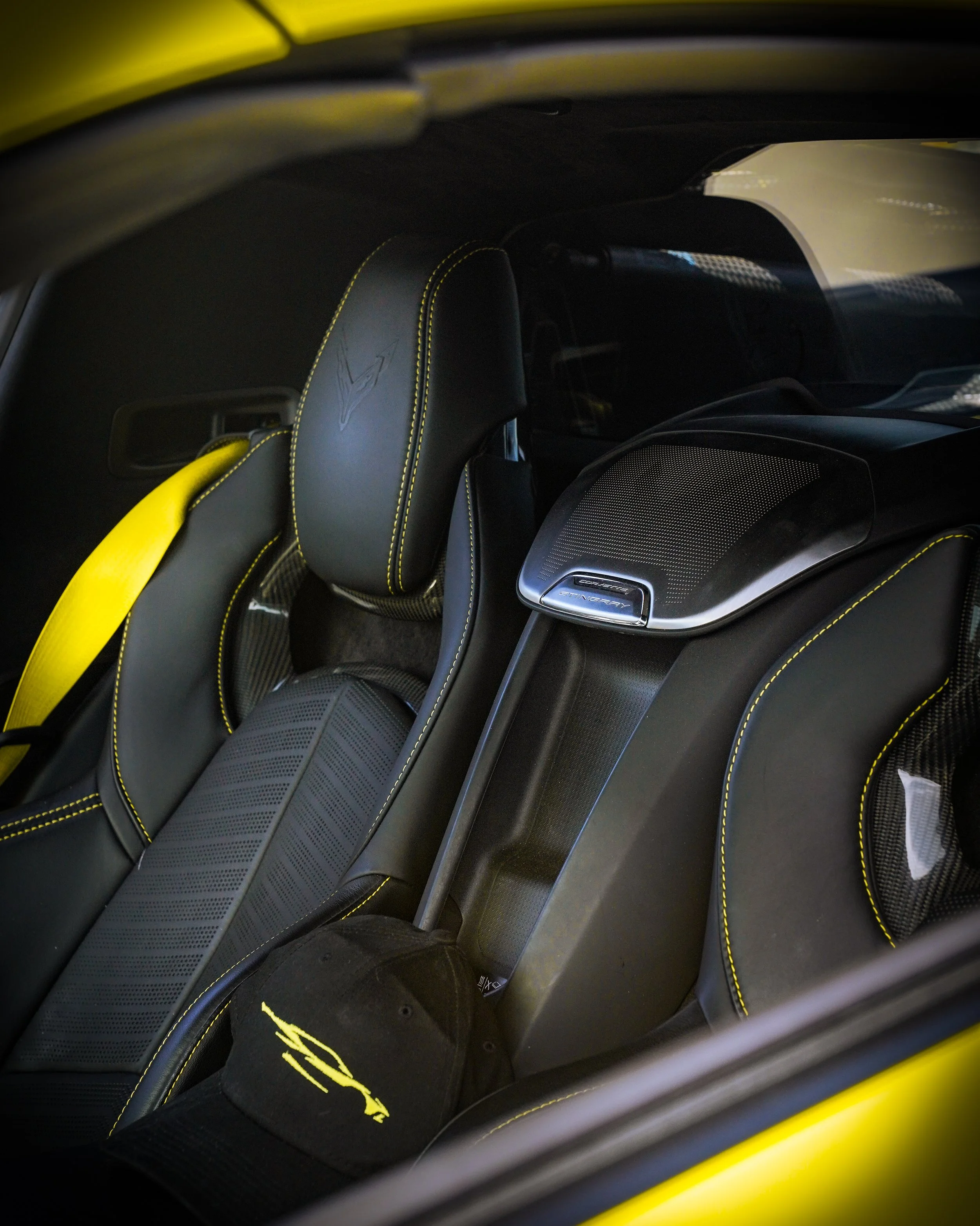 Close-up of the interior of a yellow sports car, showing black leather seats with yellow stitching and a black cap with yellow logo resting on the seat.
