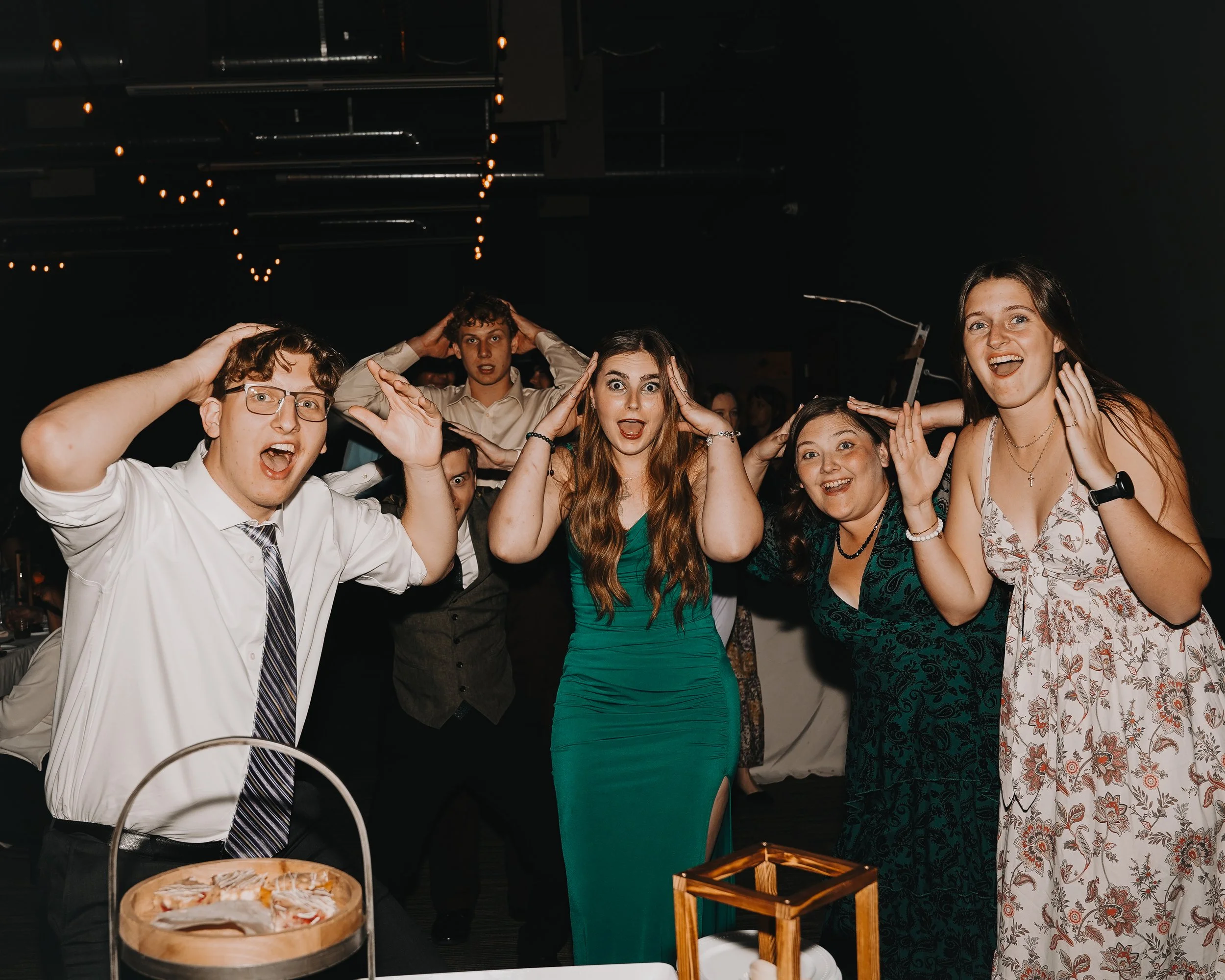 Group of five adults at a party smiling and holding their hands to their heads in a playful manner.