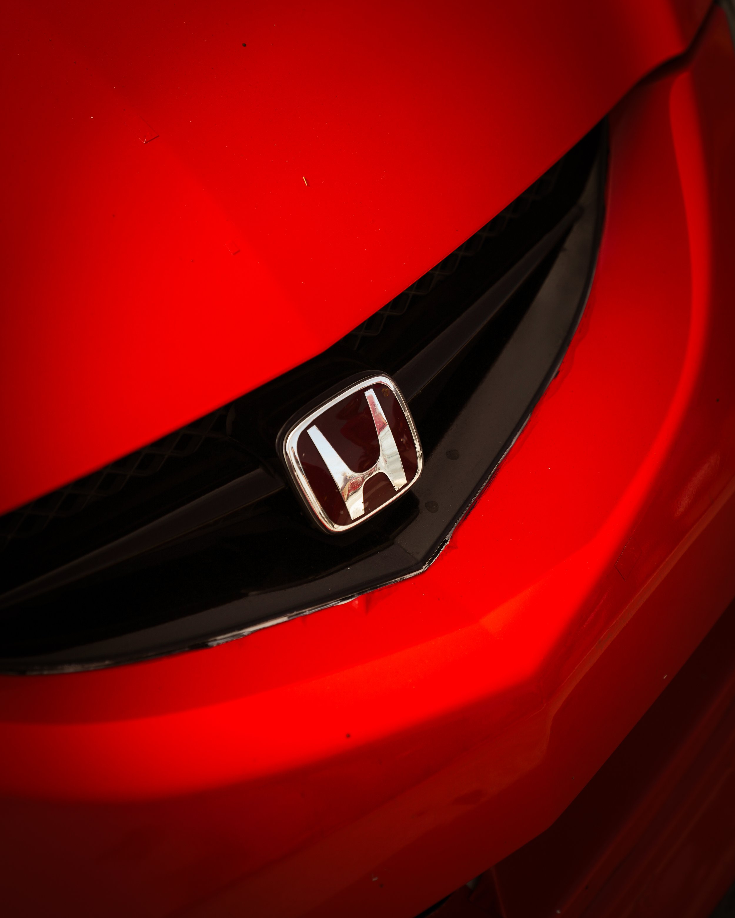 Close-up view of the front of a red Honda car, showing the Honda emblem on the grille.