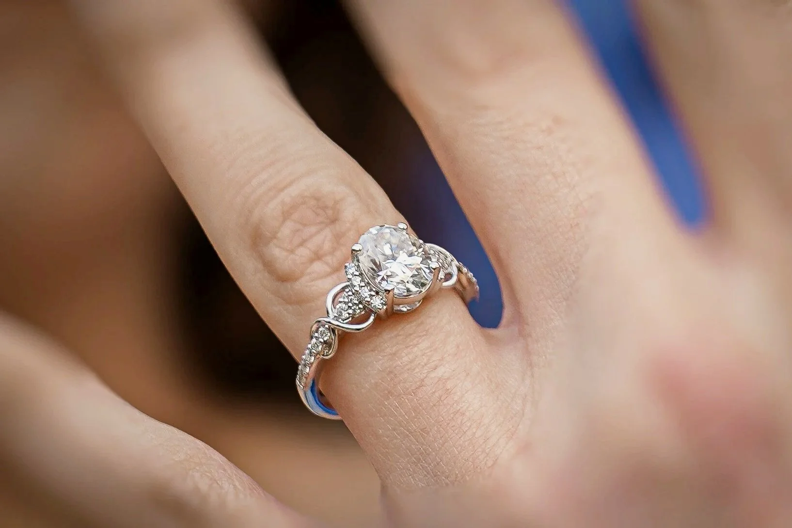 Close-up of a hand wearing a silver ring with a large oval diamond and smaller diamonds on the band.