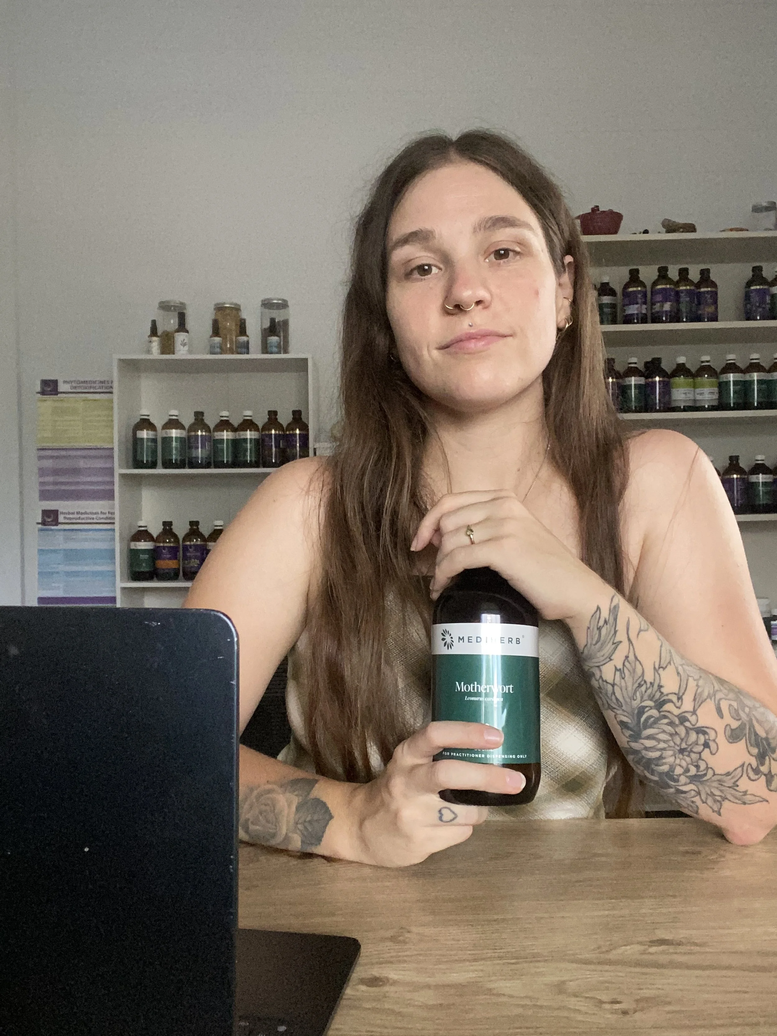 POTS-focused naturopath holding herbal medicine at her desk with a laptop in front of her