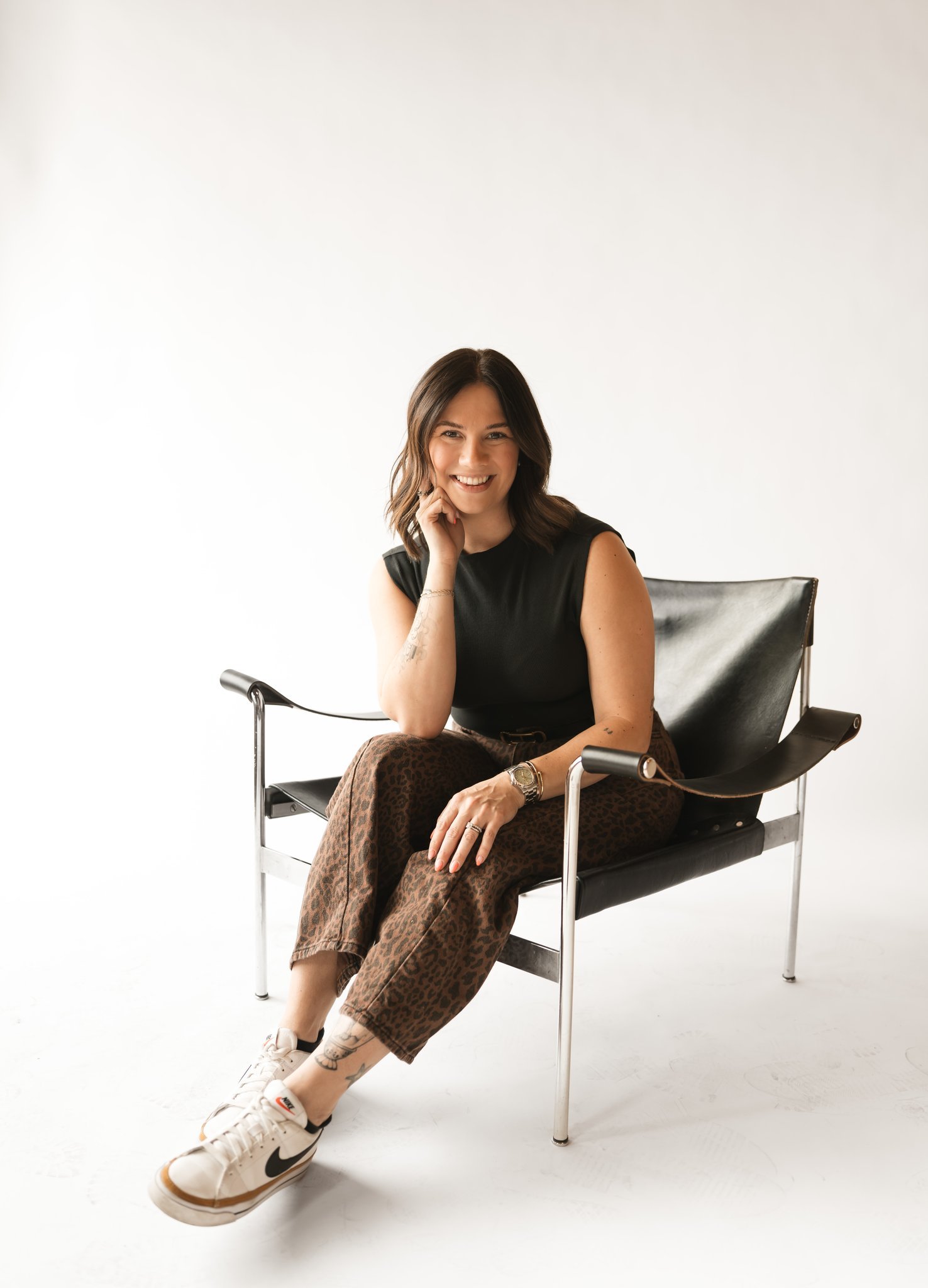 Phoenix Therapist A young woman with shoulder-length wavy brown hair, smiling, standing with her arms crossed, wearing a black shirt against a plain white background.