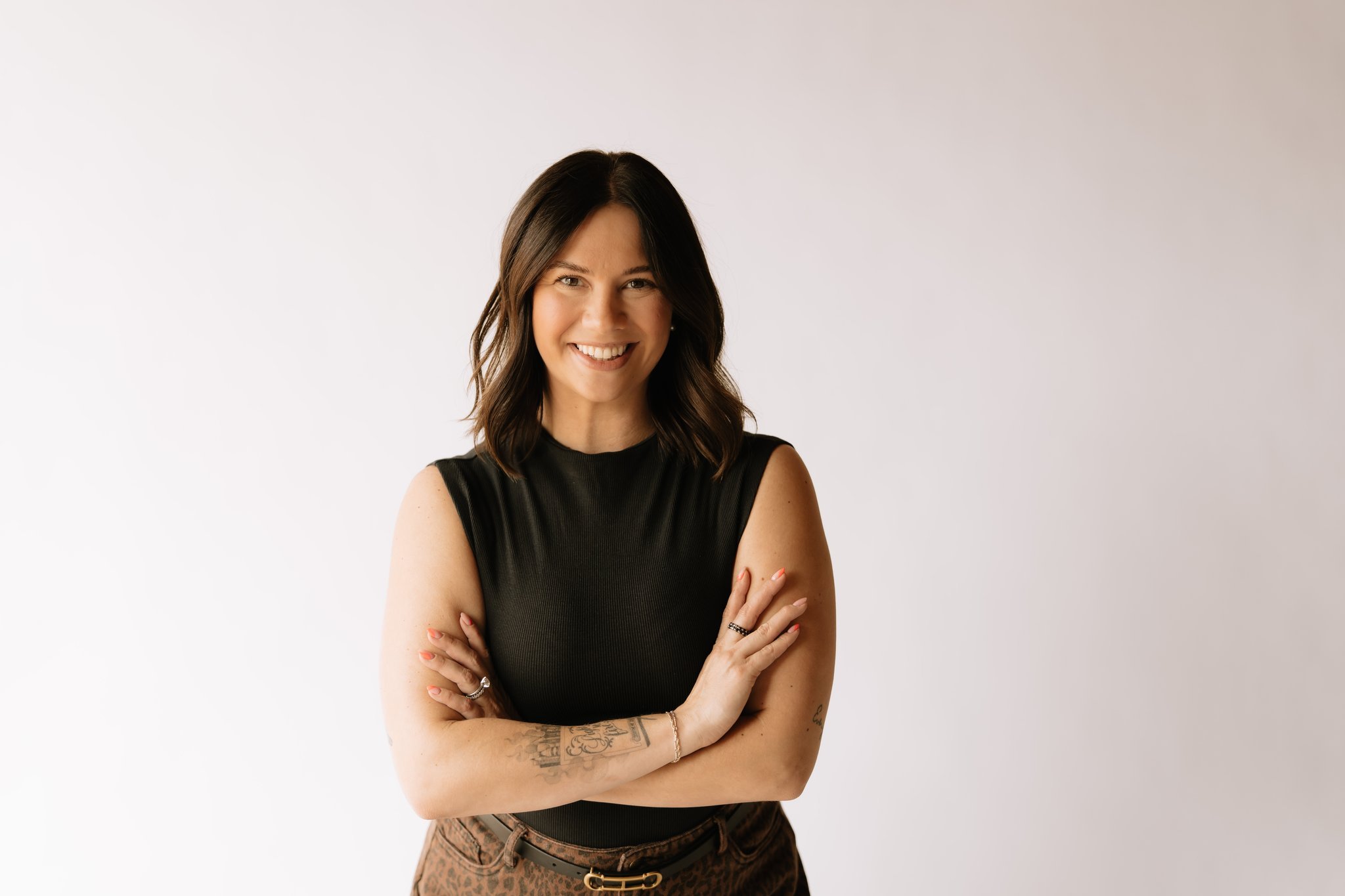  Phoenix Therapist A young woman with shoulder-length wavy brown hair, smiling, standing with her arms crossed, wearing a black shirt against a plain white background.