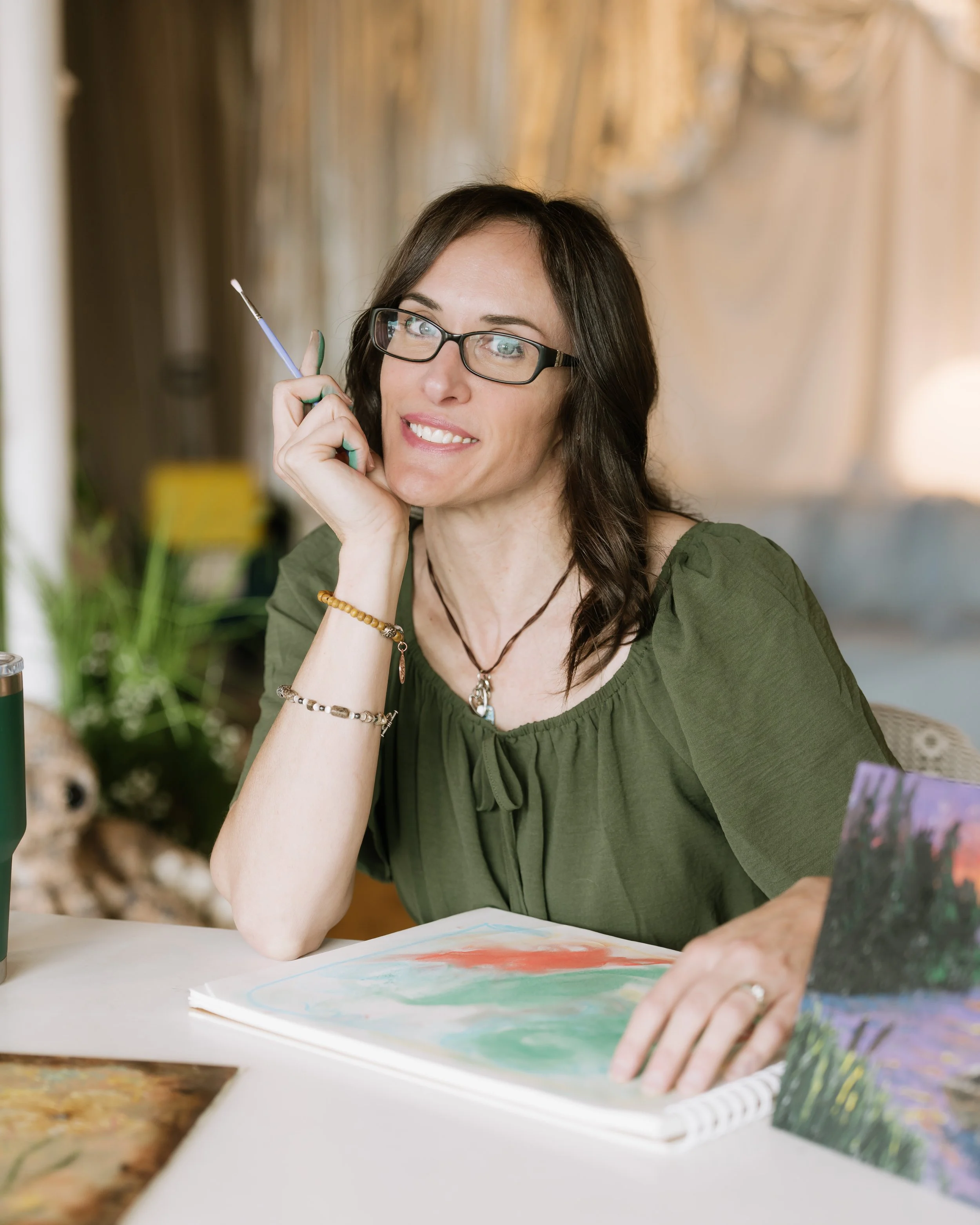  Phoenix Therapist A woman with curly brown hair, glasses, and a white button-up shirt standing against a light-colored wall, smiling at the camera.