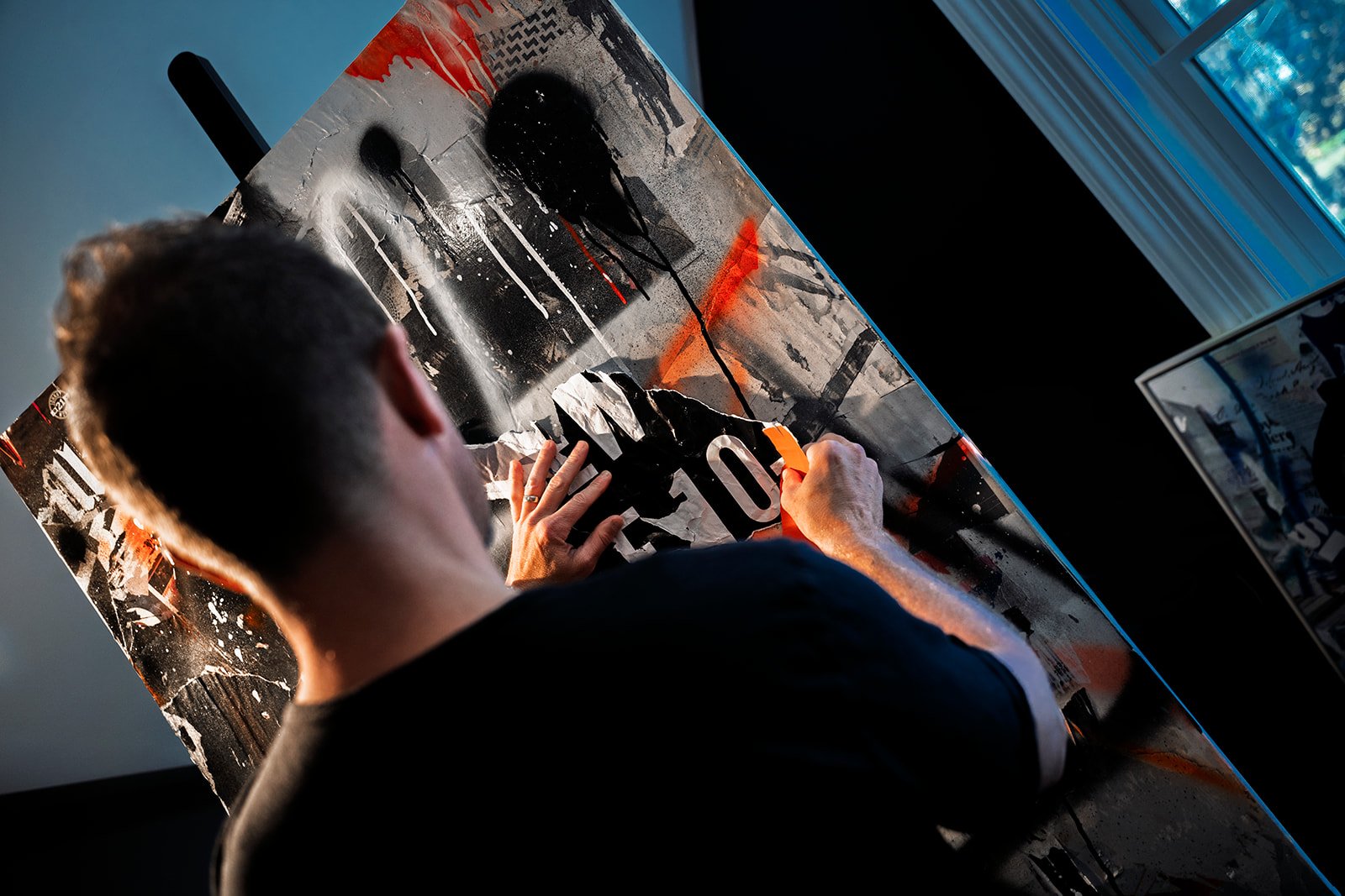 Artist creating a mixed media artwork with black, white, and orange colors in a studio environment.