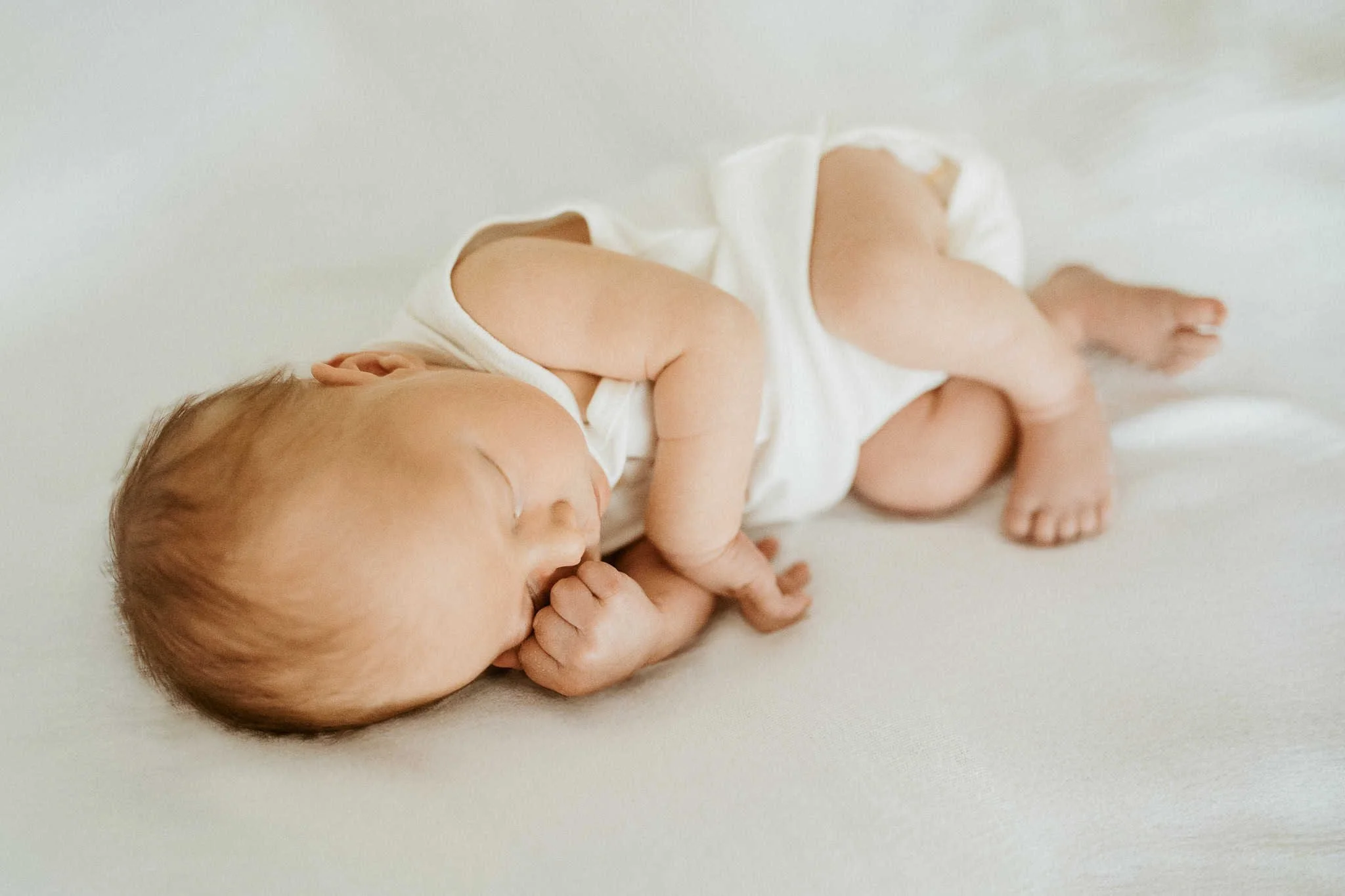 Baby on white bedsheet photographed by newborn photographer in zürich