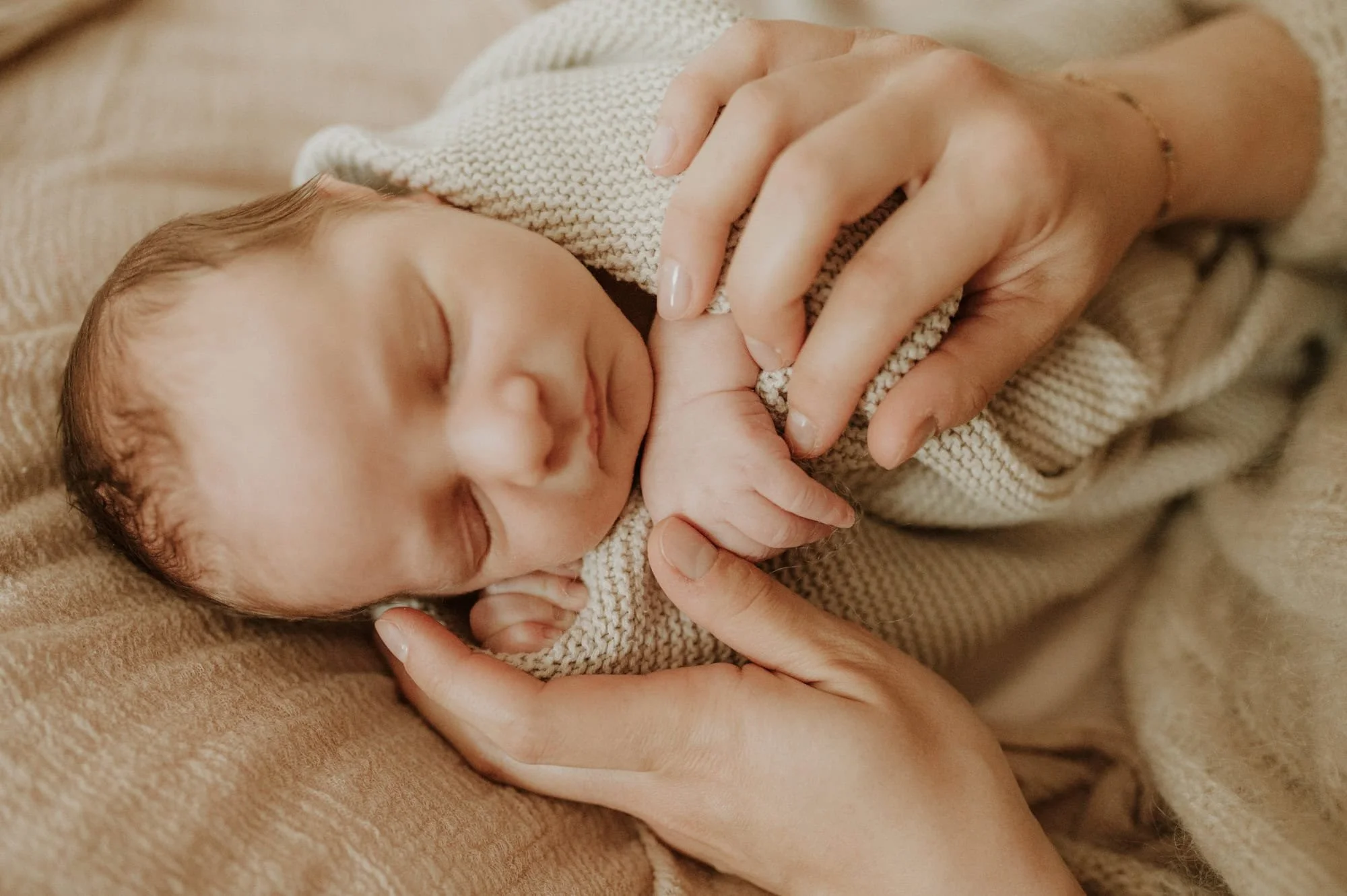 Newborn wrapped snugly in delicate fabrics with the mother’s hands resting gently on top.
