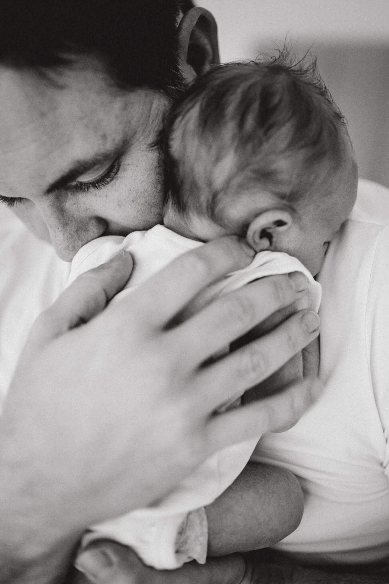 Black and white portrait of a father gently kissing his newborn baby on the forehead during a newborn session in Zürich.