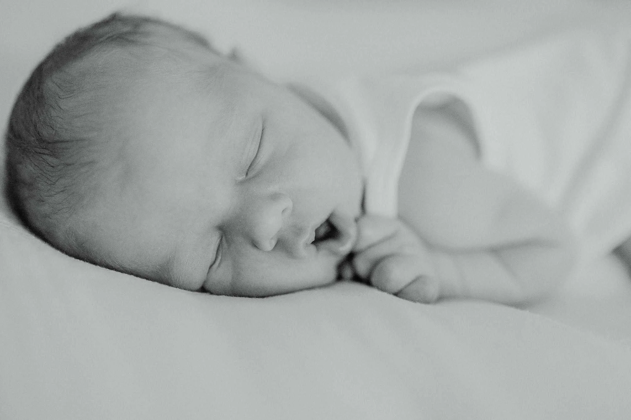 Black and white newborn portrait of a sleeping baby lying on its side with hands near the face during a newborn session.