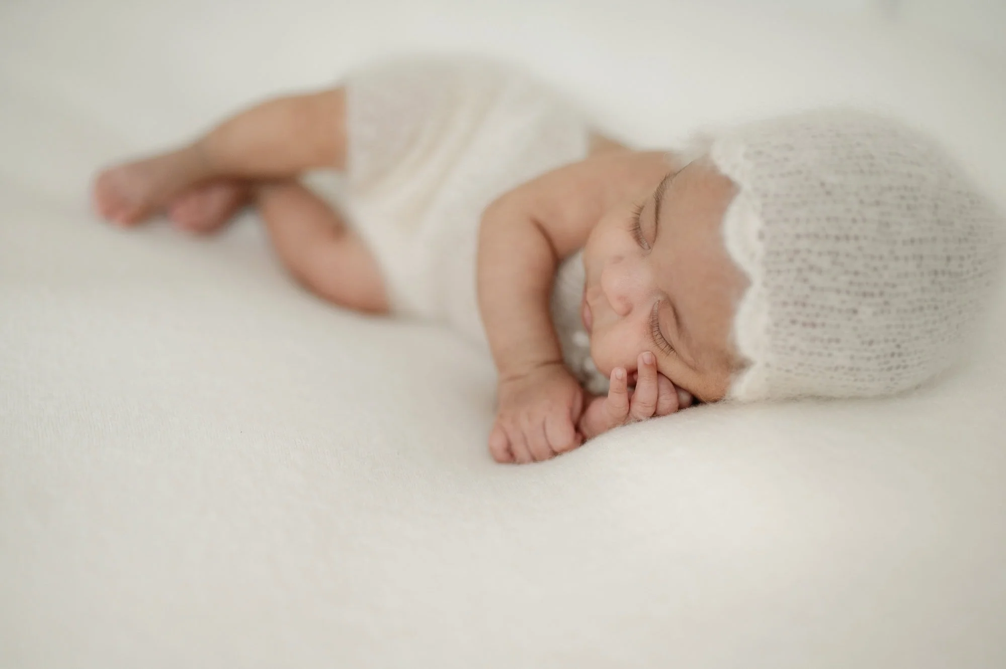 Schlafendes Neugeborenes in hellen Weißtönen; ein minimalistisches Newborn-Portrait.
