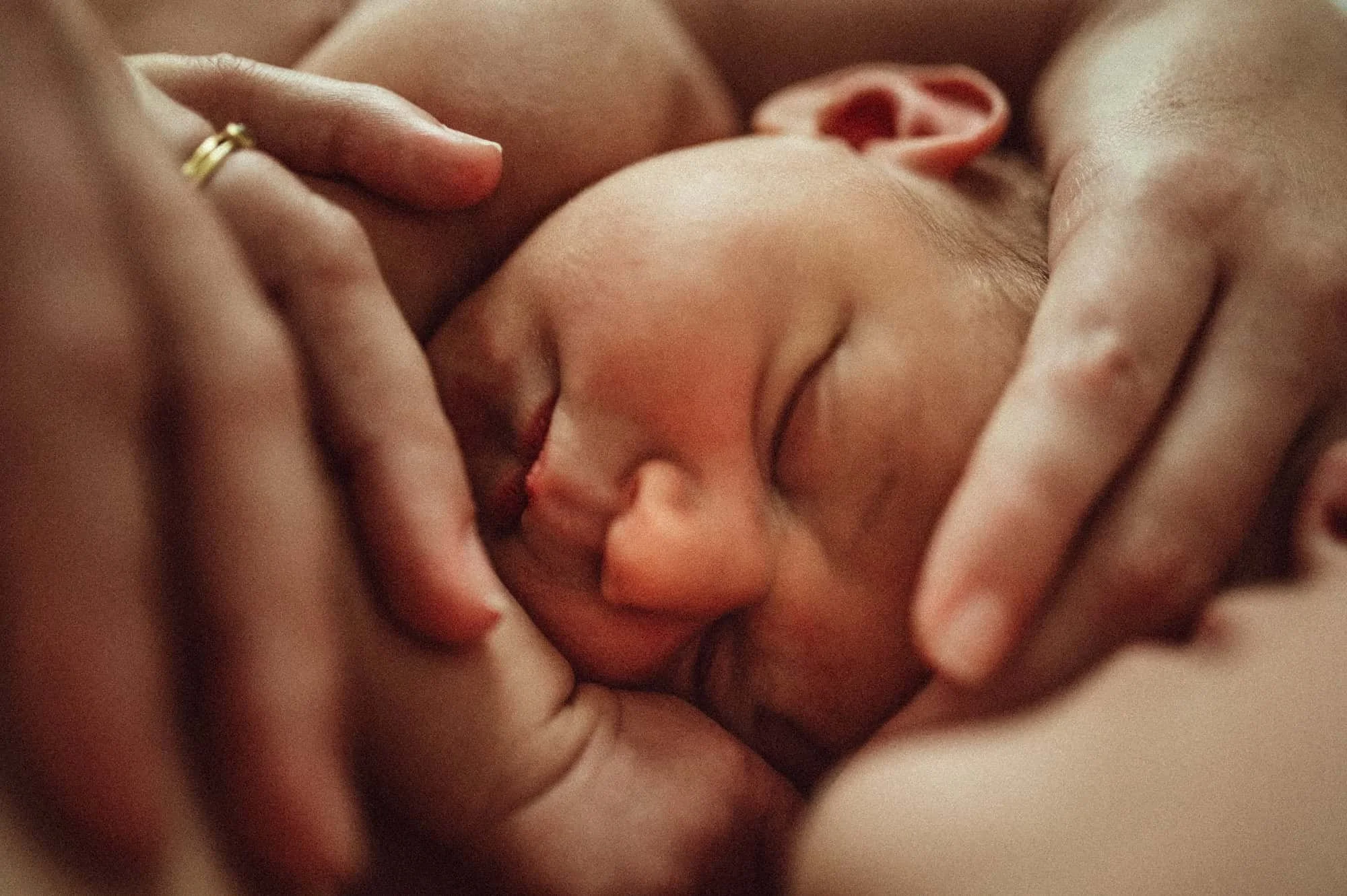 Neugeborenes Baby in einer innigen Umarmung mit seiner Mutter, festgehalten von der besten Neugeborenenfotografin in Zürich, voller Wärme und Geborgenheit.