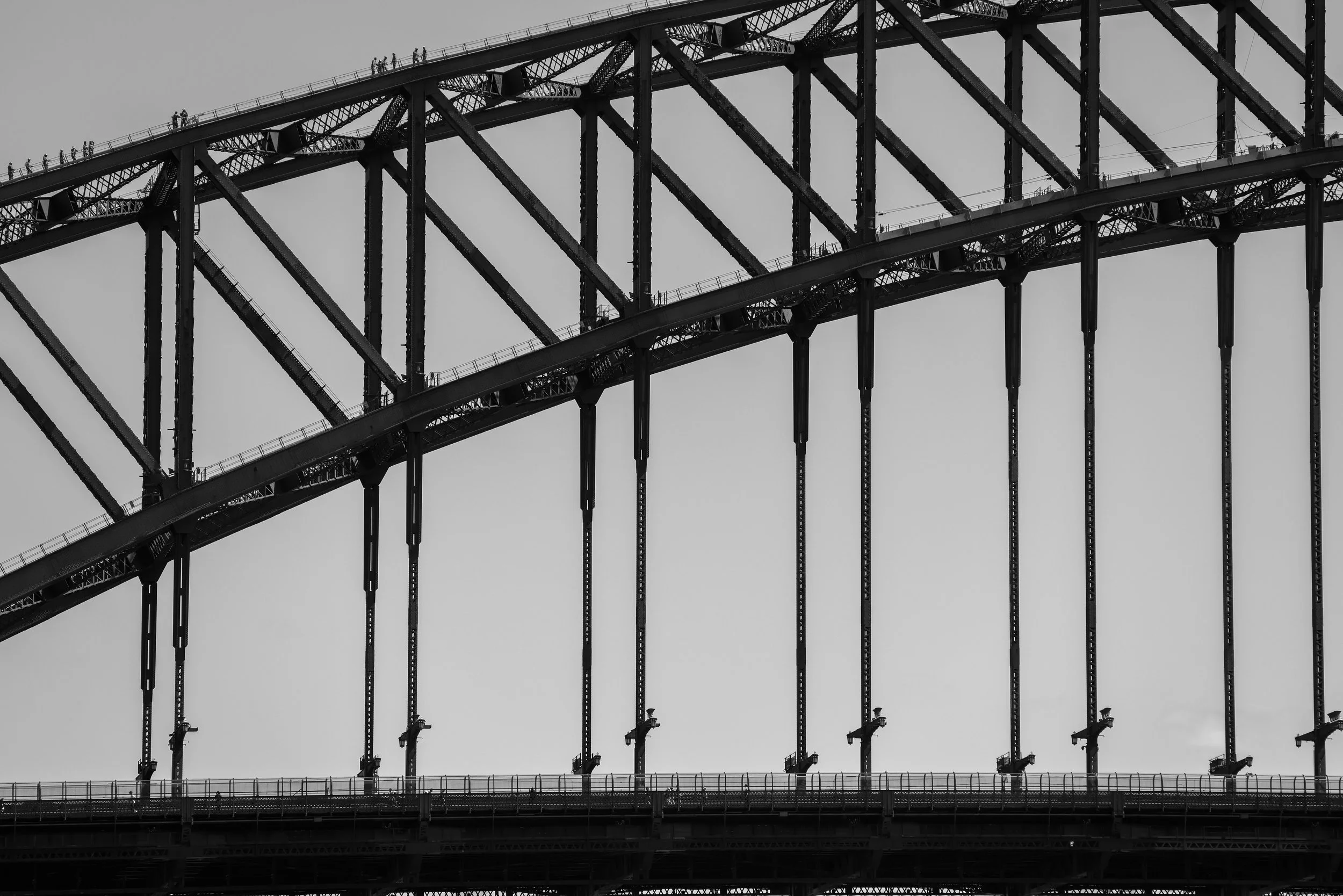 Close-up of the Sydney Harbour Bridge in black and white, showing its steel arch and structure with maintenance work happening underneath.
