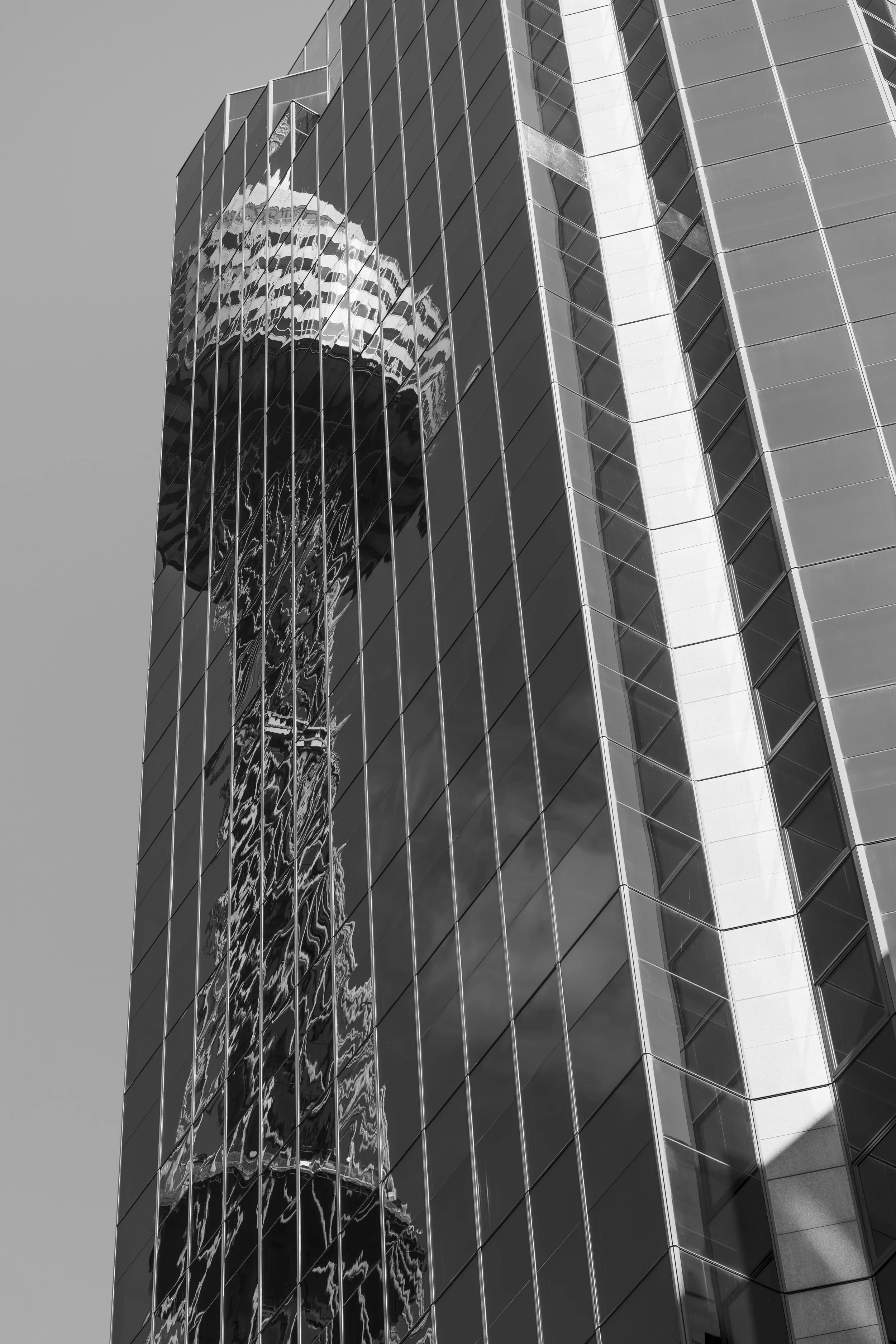 A modern skyscraper with reflective glass windows, reflecting another building's patterns and the sky.