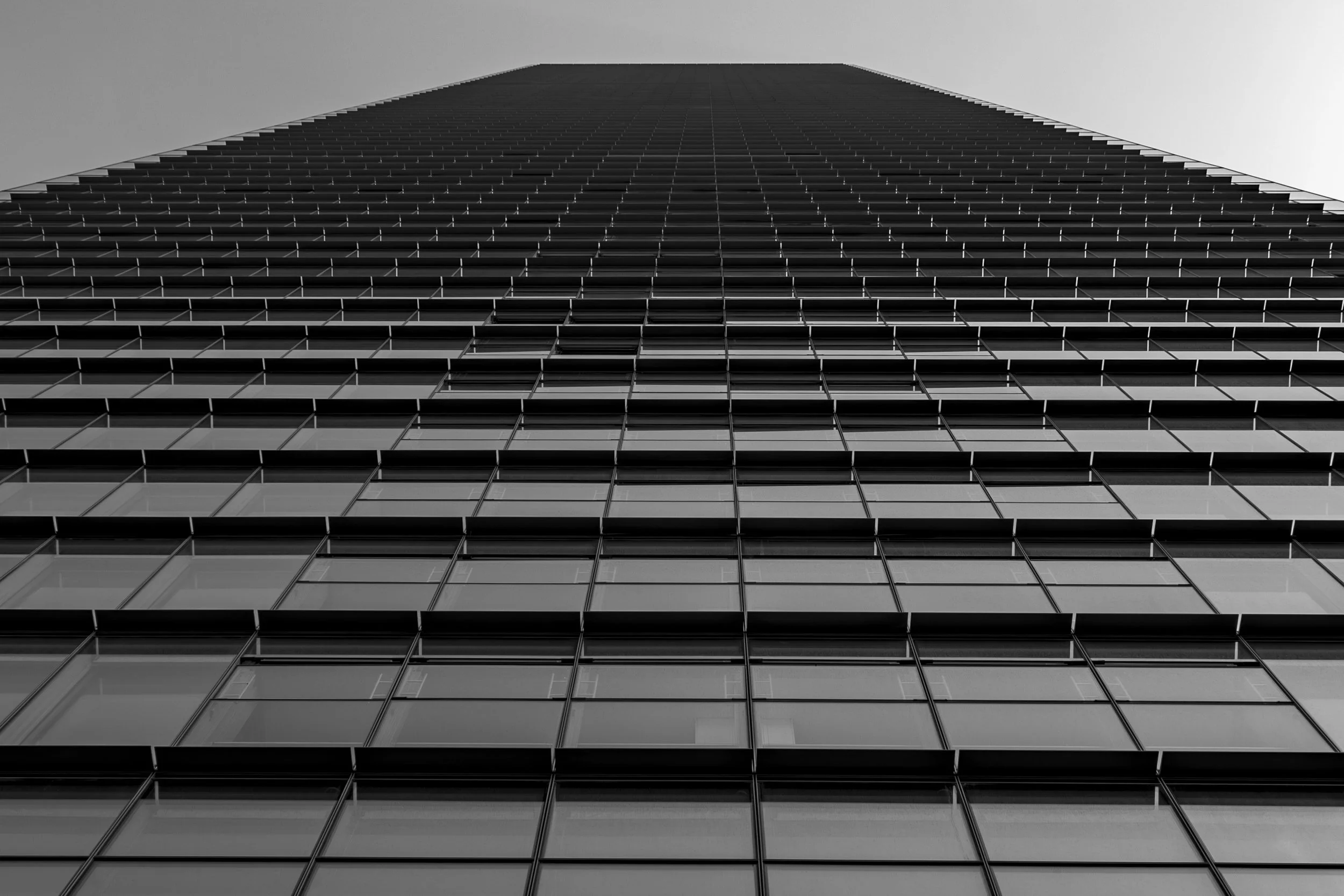 Low-angle view of a tall modern skyscraper with glass windows against a cloudy sky.