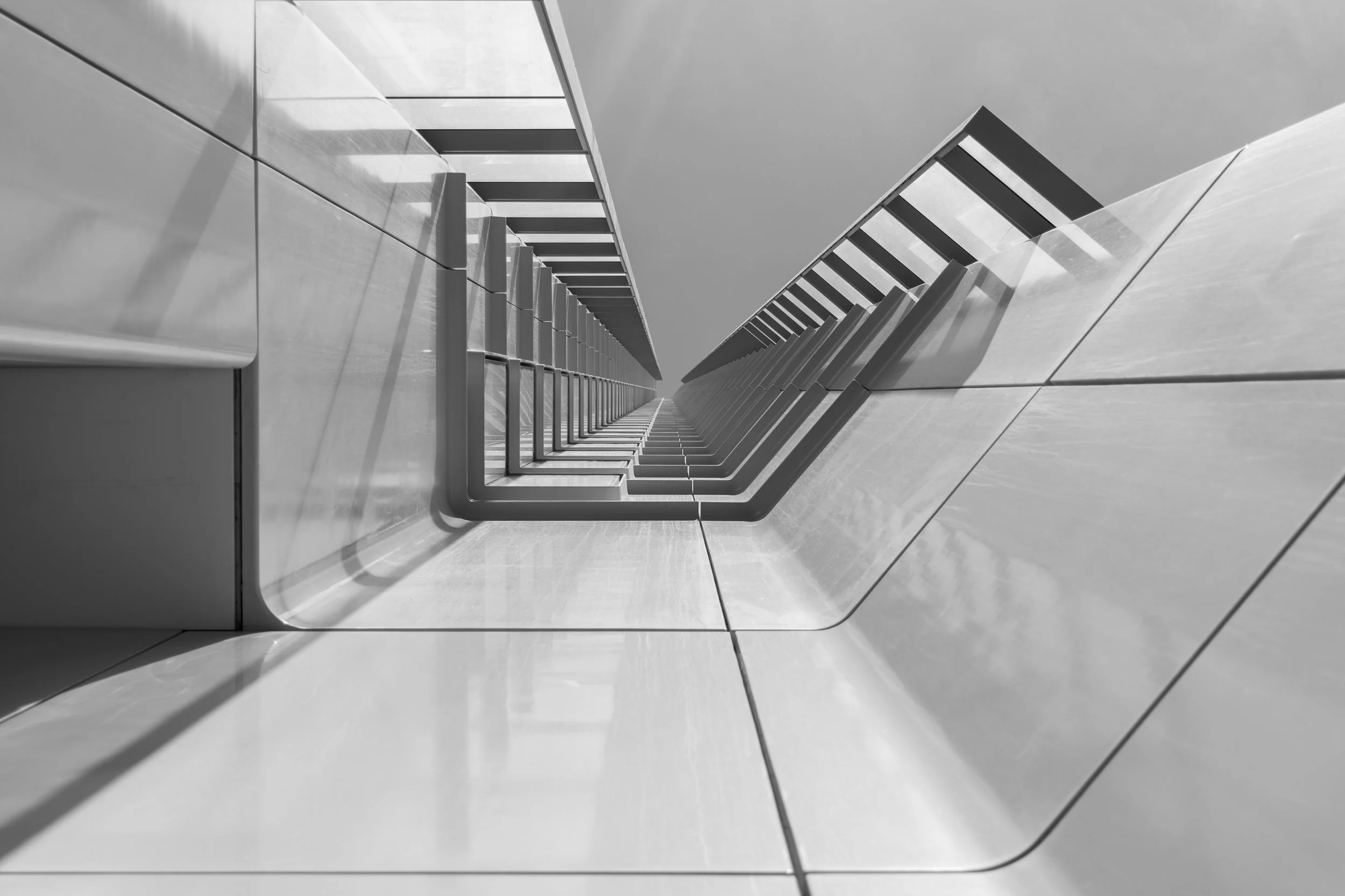 Black and white photograph of an architectural structure viewed from below, showcasing diagonal lines and geometric shapes.