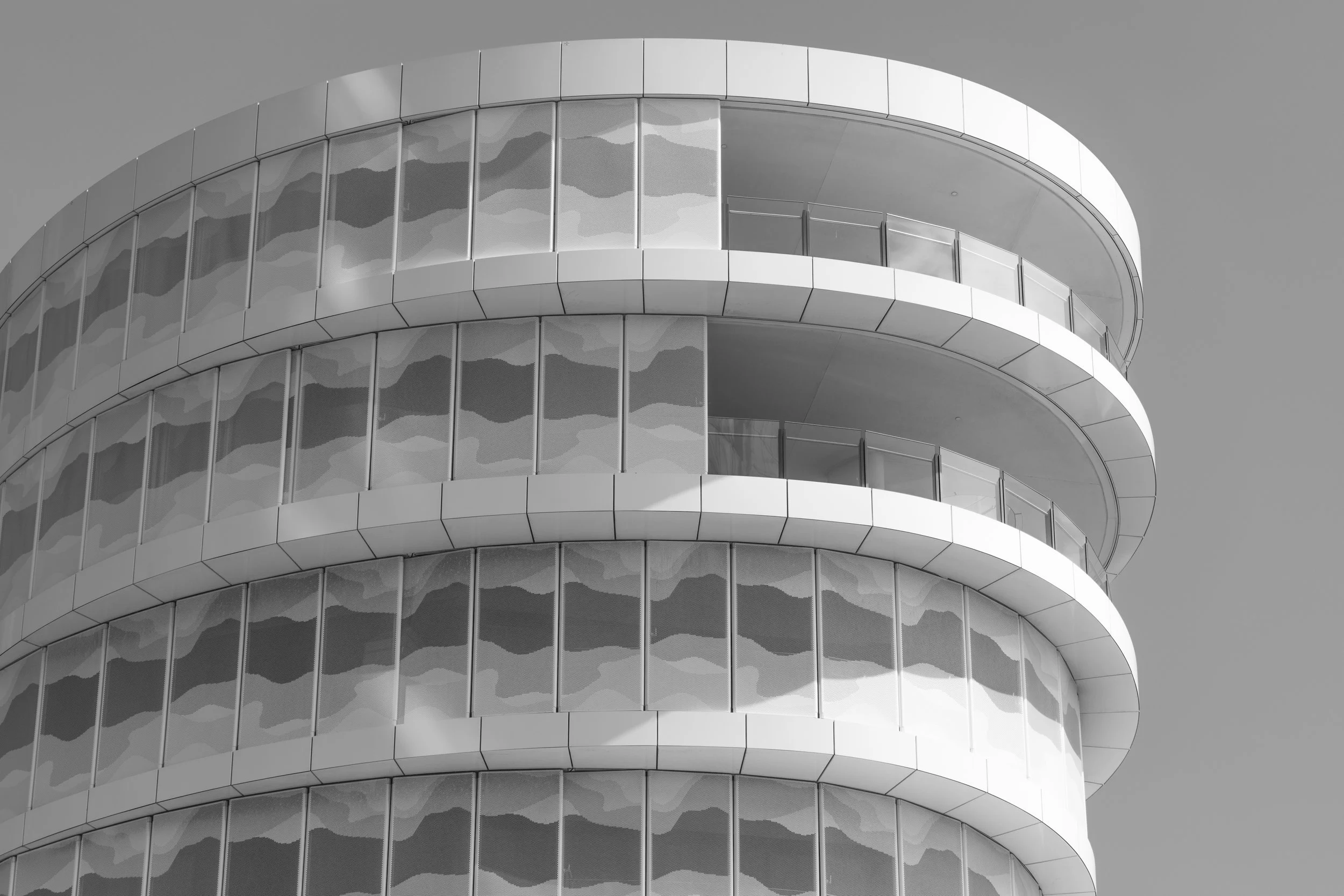 A modern, curved building with multiple floors, featuring reflective glass windows and rounded balconies in grayscale.