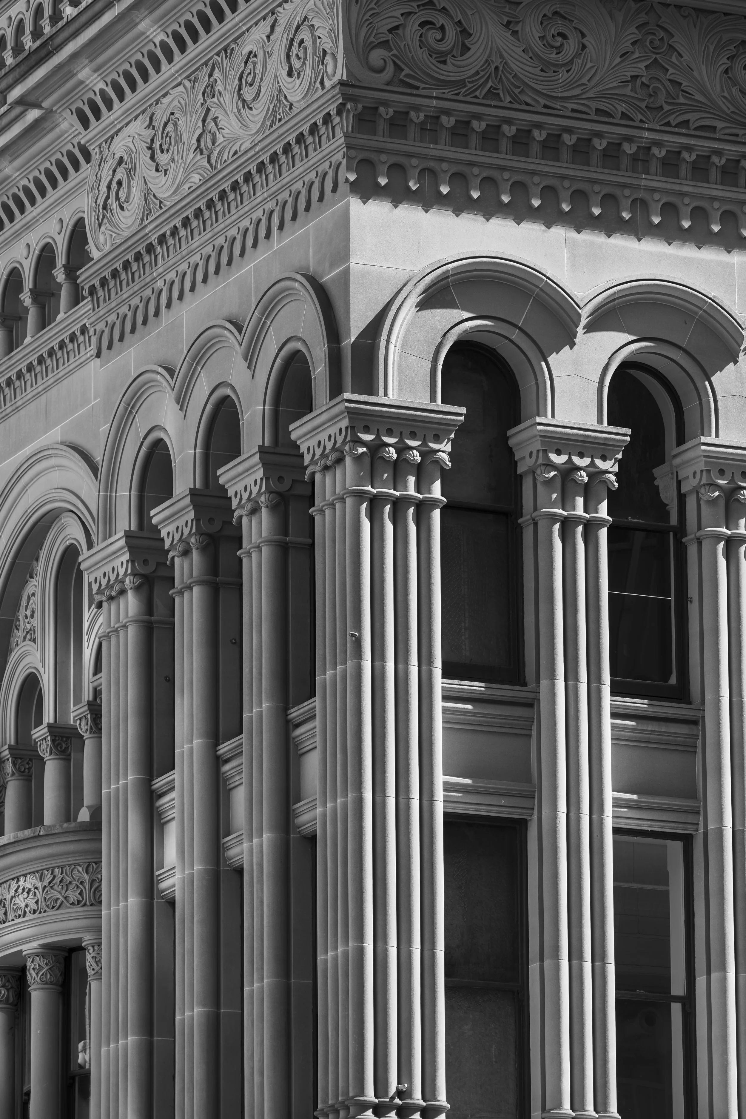 Close-up of a historic building's ornate architectural details, including arched windows with decorative molding and tall columns with detailed capitals, in black and white.