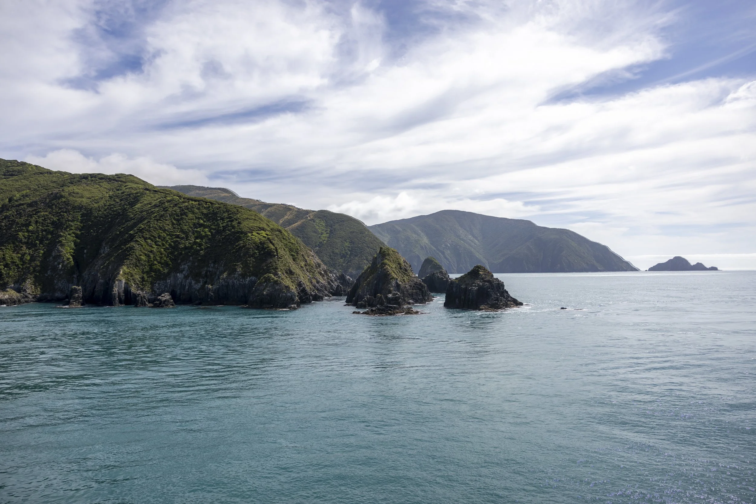Scenic view of green coastal cliffs with rocky formations extending into the ocean, under a partly cloudy sky.
